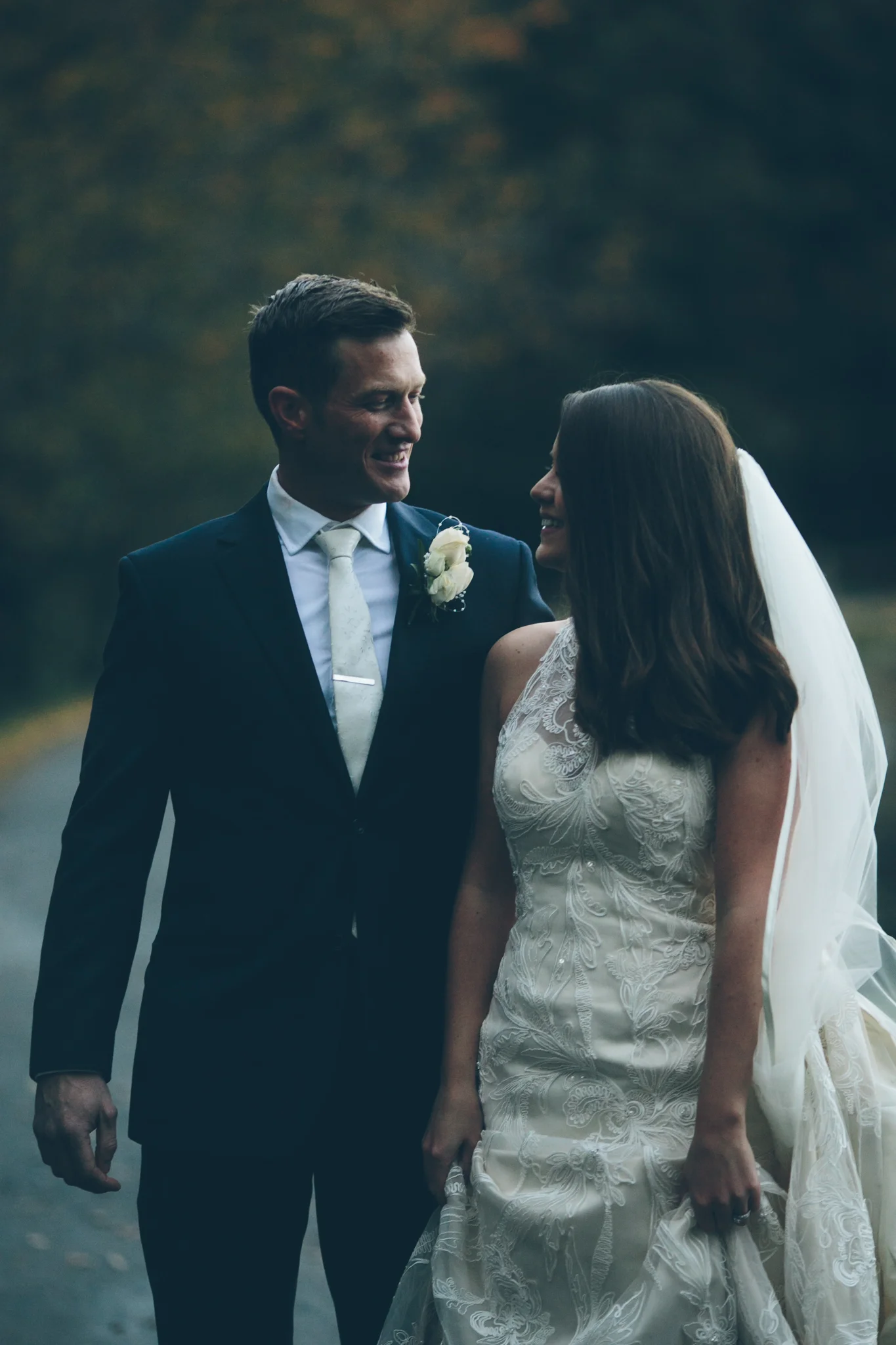 A bride and groom smiling at each other outdoors during their wedding.