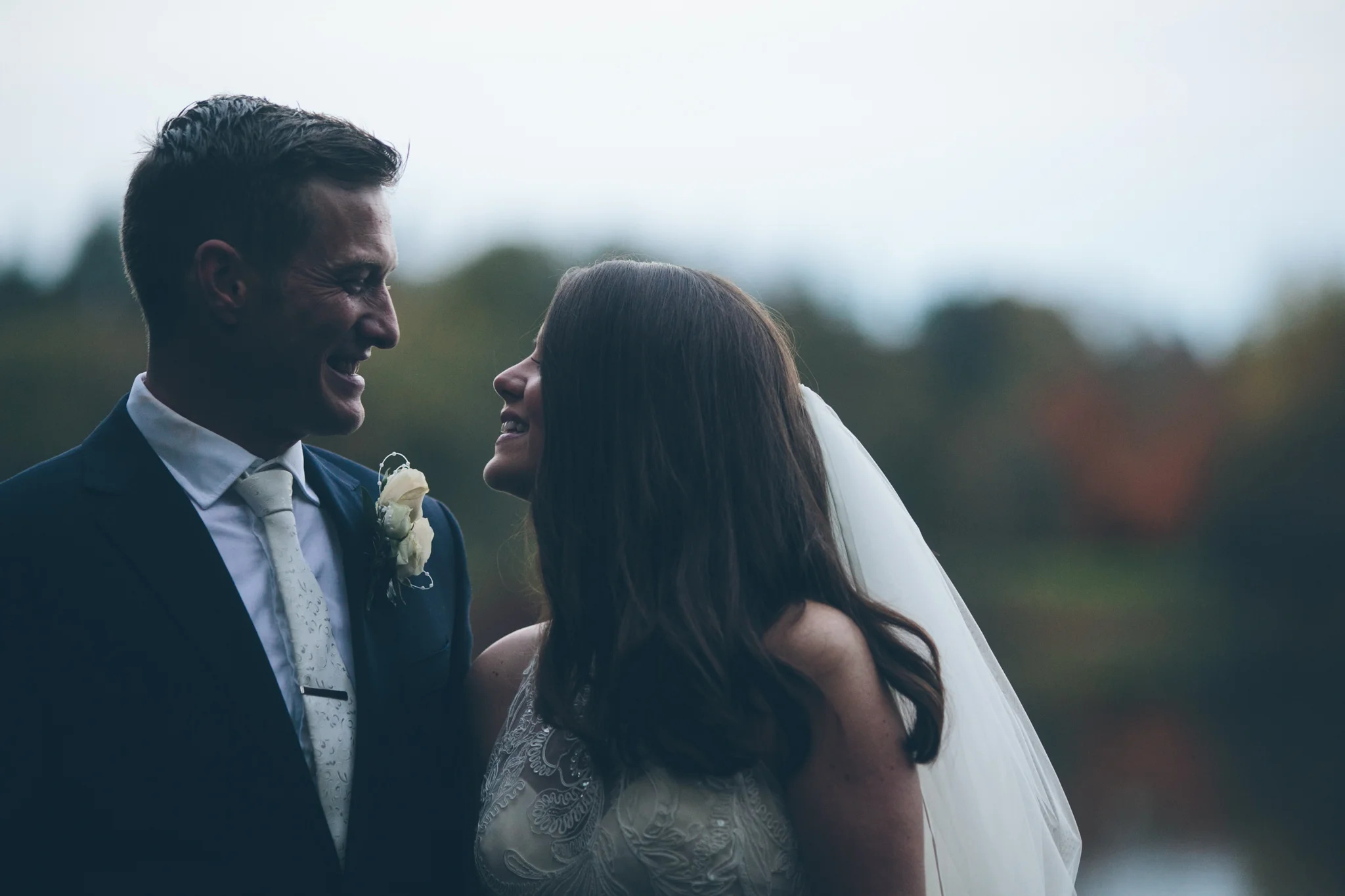 A bride and groom smiling at each other outdoors during their wedding.