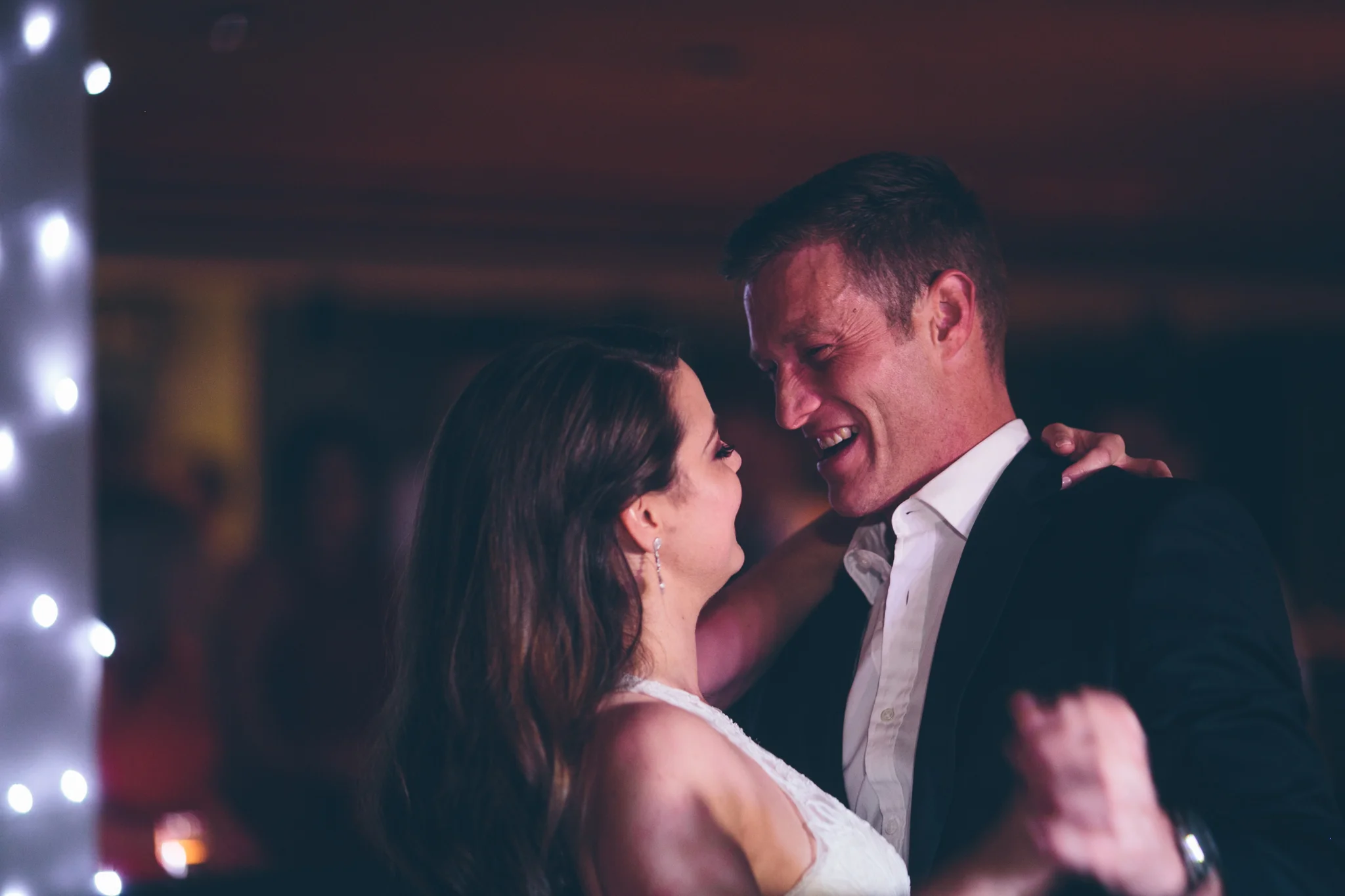 A bride and groom share a dance at their wedding reception, smiling and enjoying a close moment.