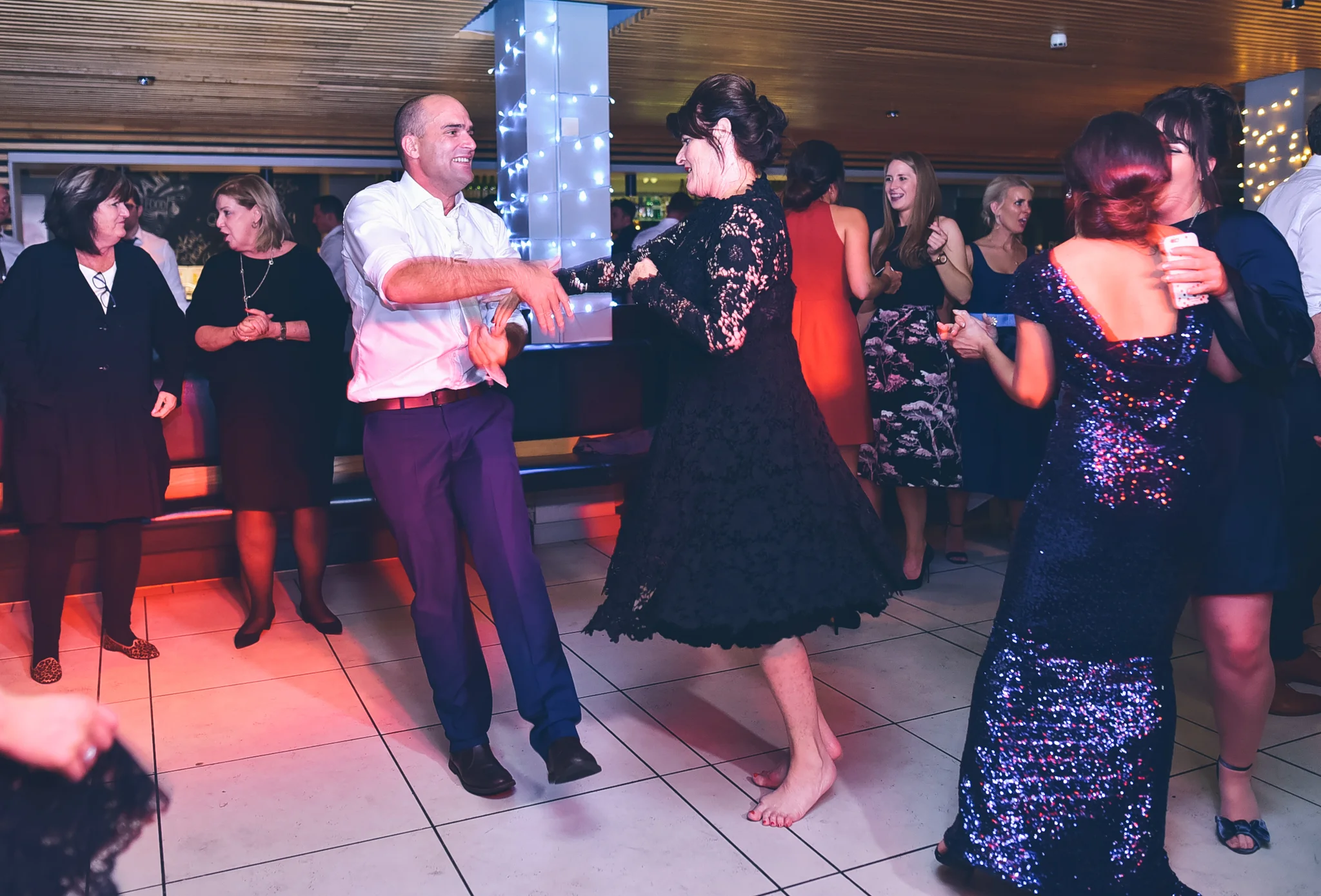 People dancing and socializing at a party in a decorated indoor venue with string lights.