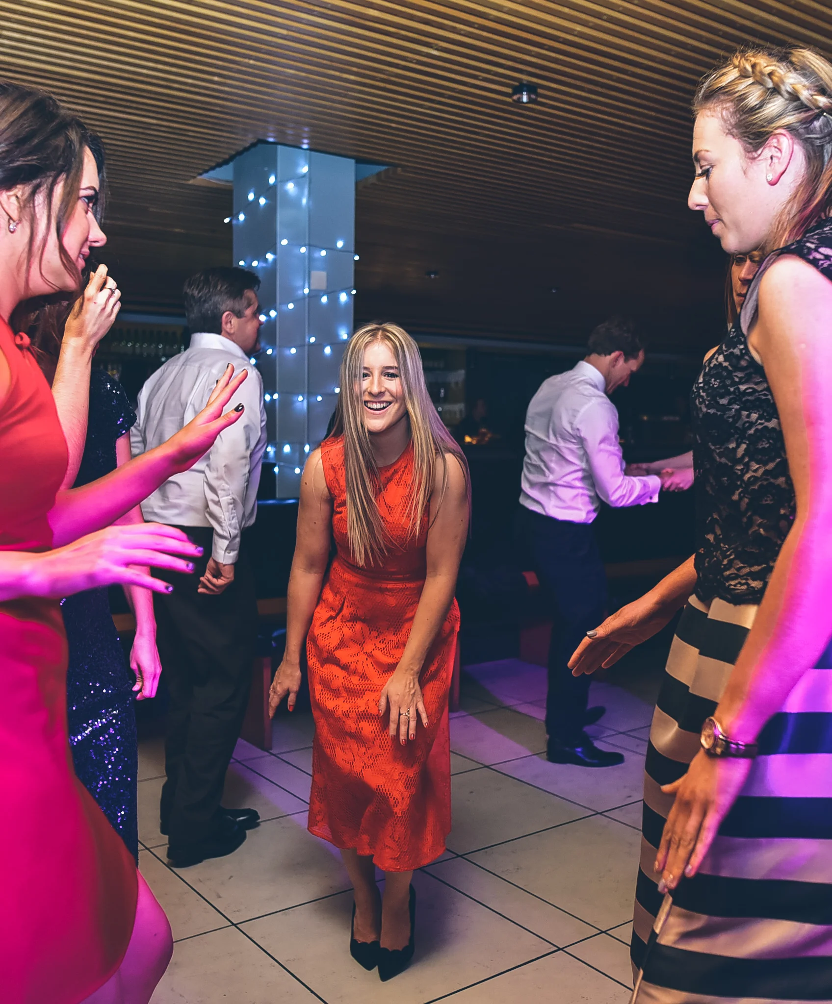 Young woman in a red dress smiling and dancing at a party with other people in the background.