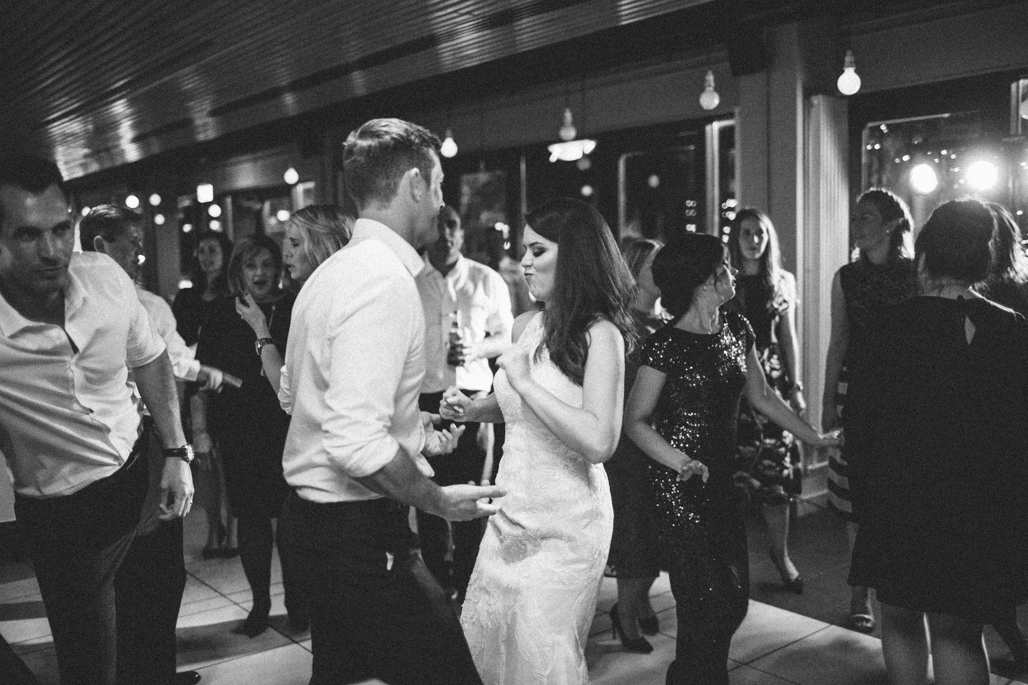 People dancing and socializing at a party or reception in a decorated indoor venue, with some wearing formal attire.