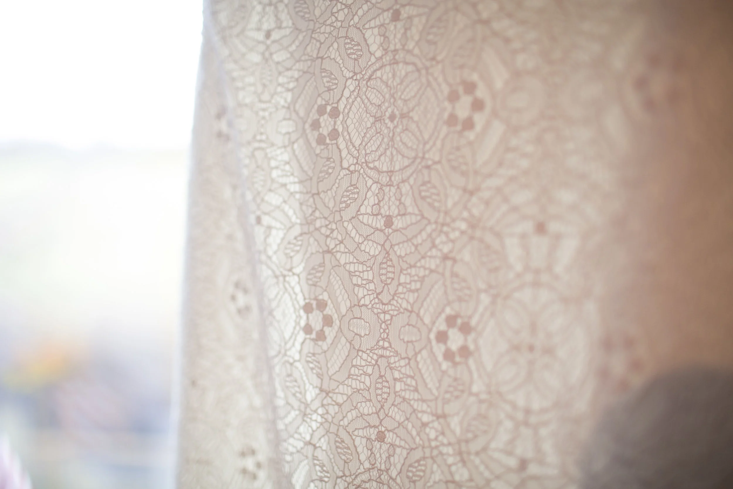 Close-up of a lace curtain with intricate floral and geometric patterns, softly illuminated by natural light.