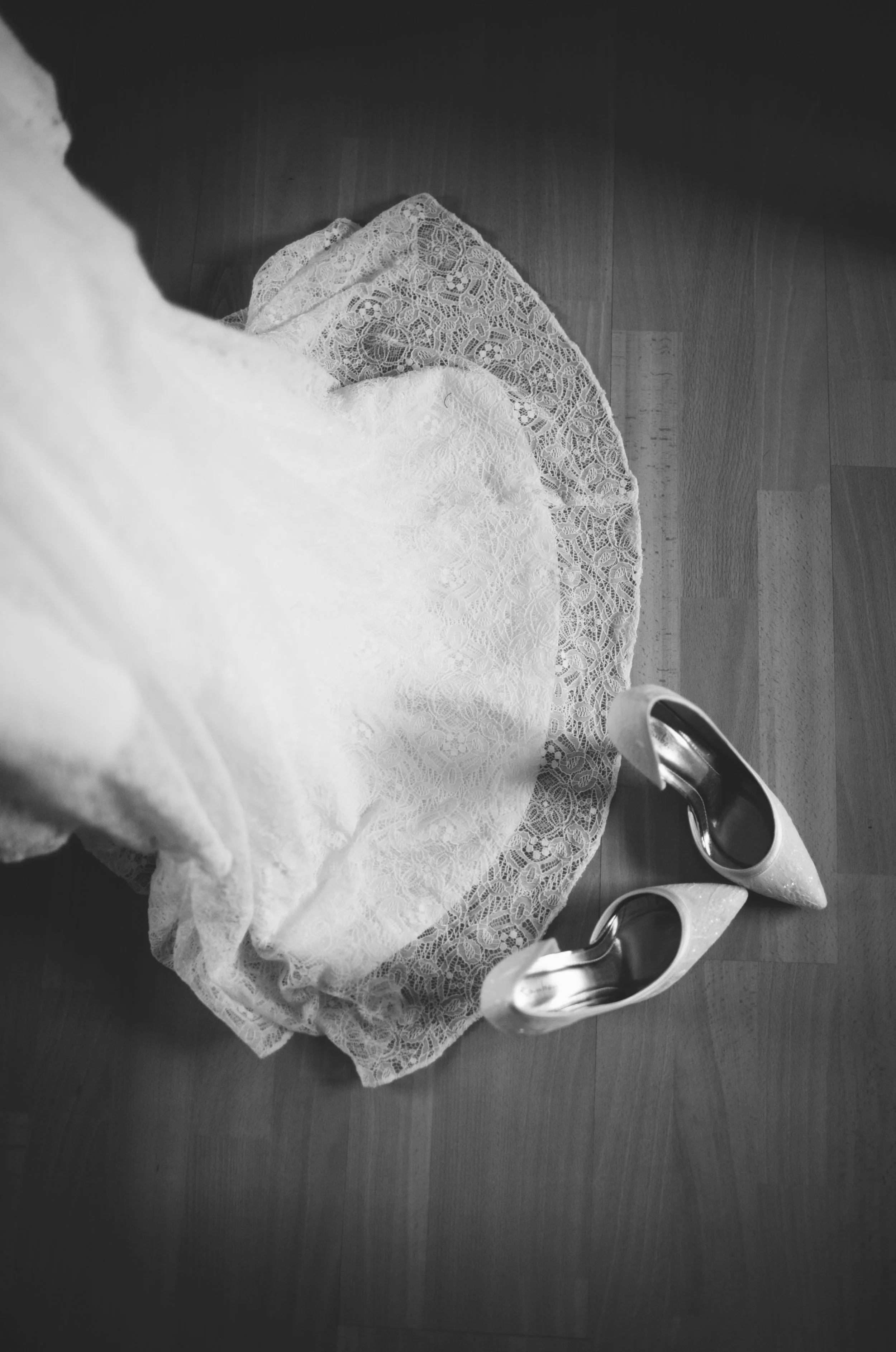 A pair of white high-heeled shoes placed on a round lace doily on a wooden floor.