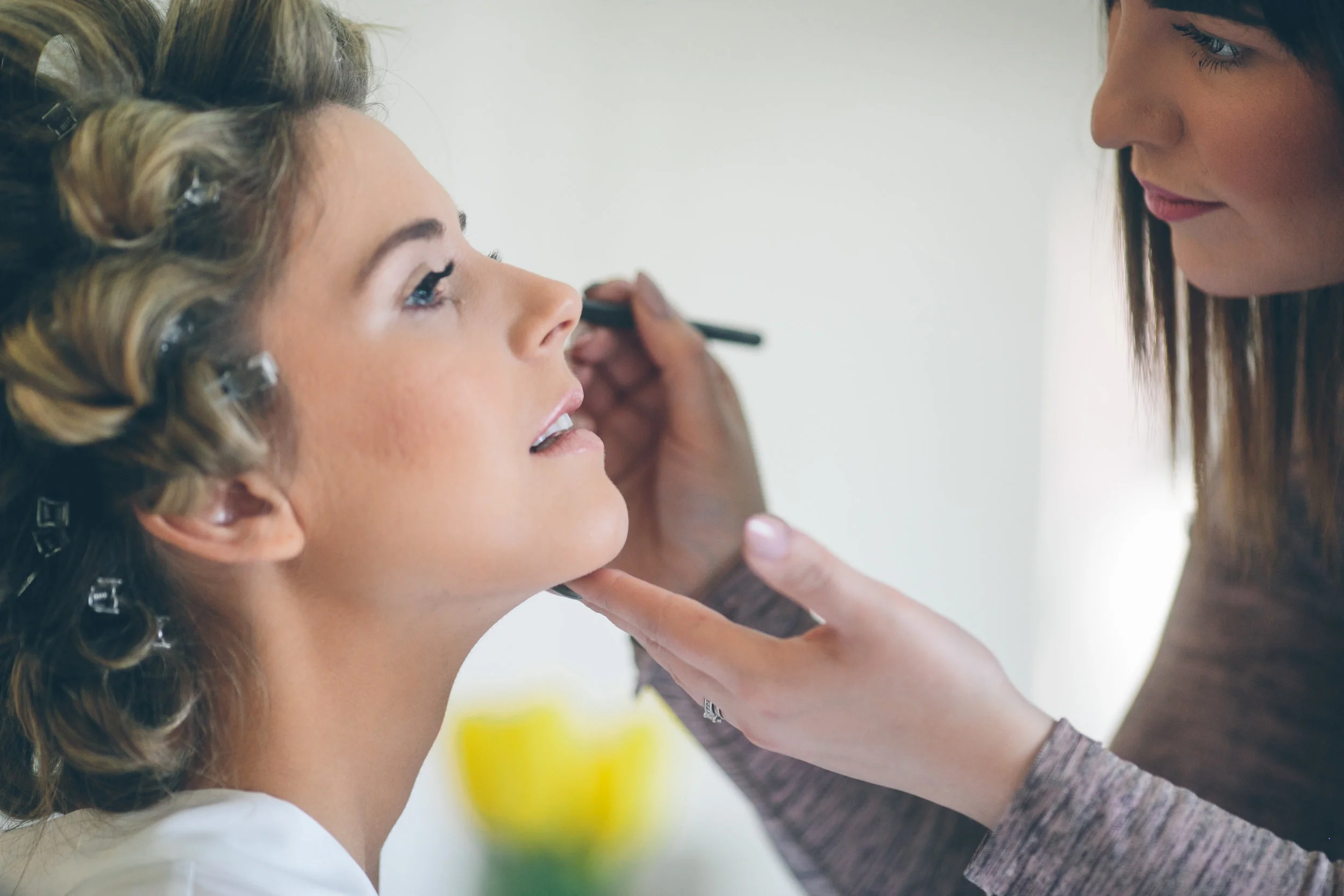 Woman applying makeup to another woman with curled hair.