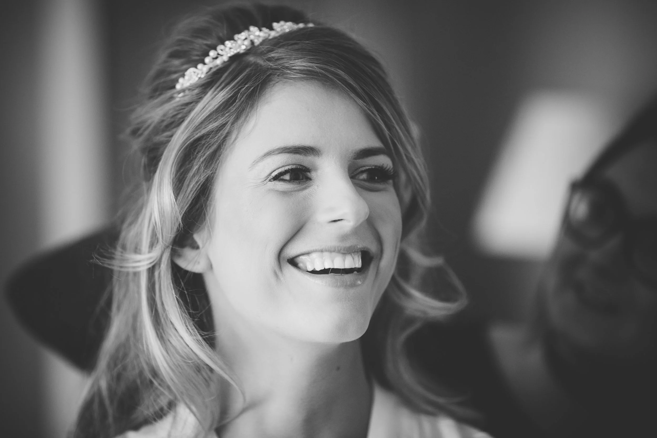 A woman smiling with a tiara in her hair, possibly a bride, getting ready.
