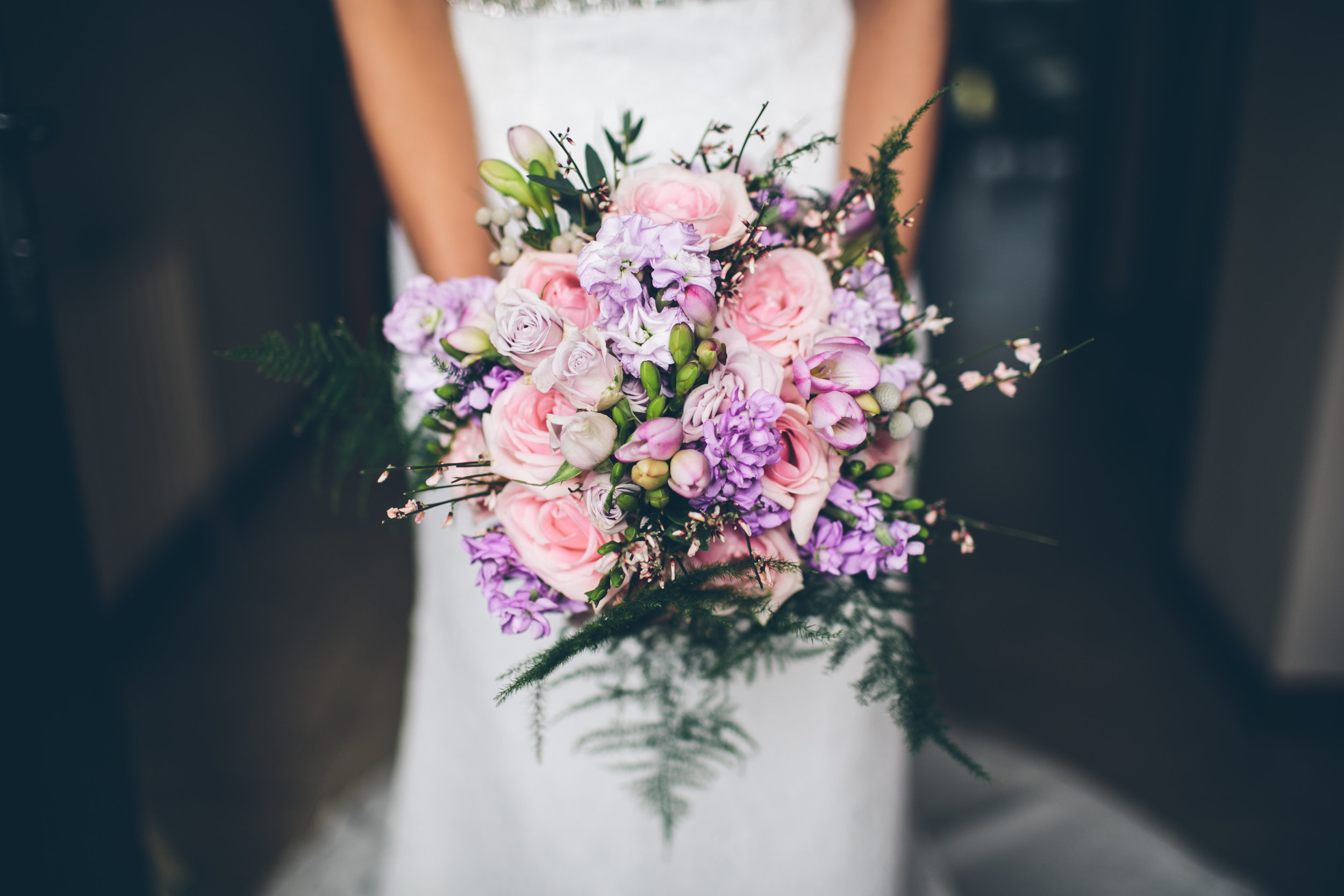 A person holding a bouquet of pink and purple flowers, including roses and other blooms, with green foliage.