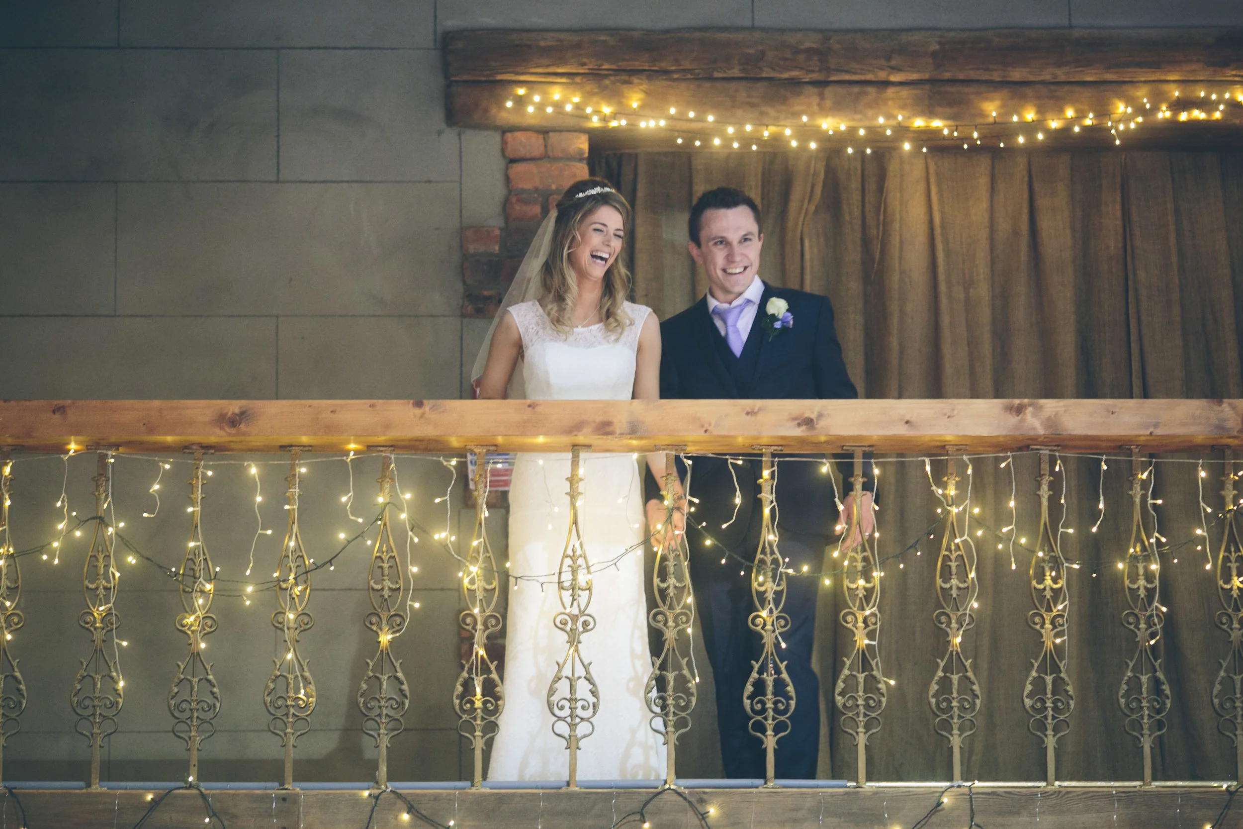 A happy bride and groom standing together on a balcony with string lights, celebrating their wedding.