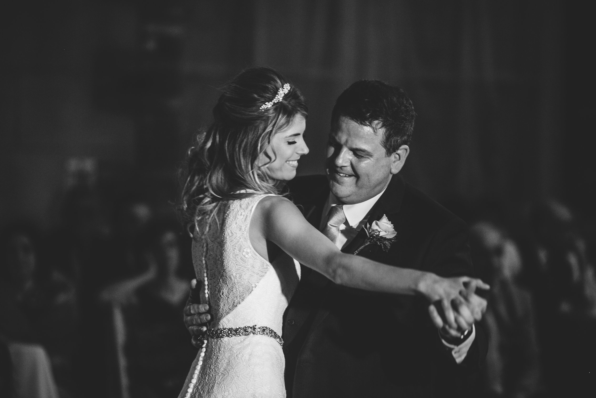 Black and white photo of a bride and groom sharing a dance at their wedding, smiling at each other.