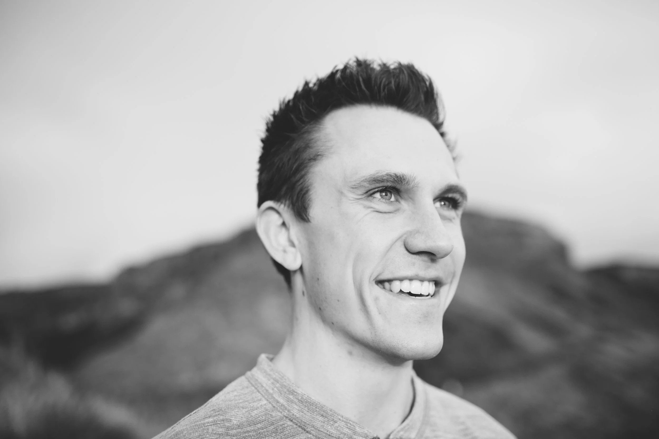A smiling young man with short dark hair looking to the side outdoors, black and white photograph.