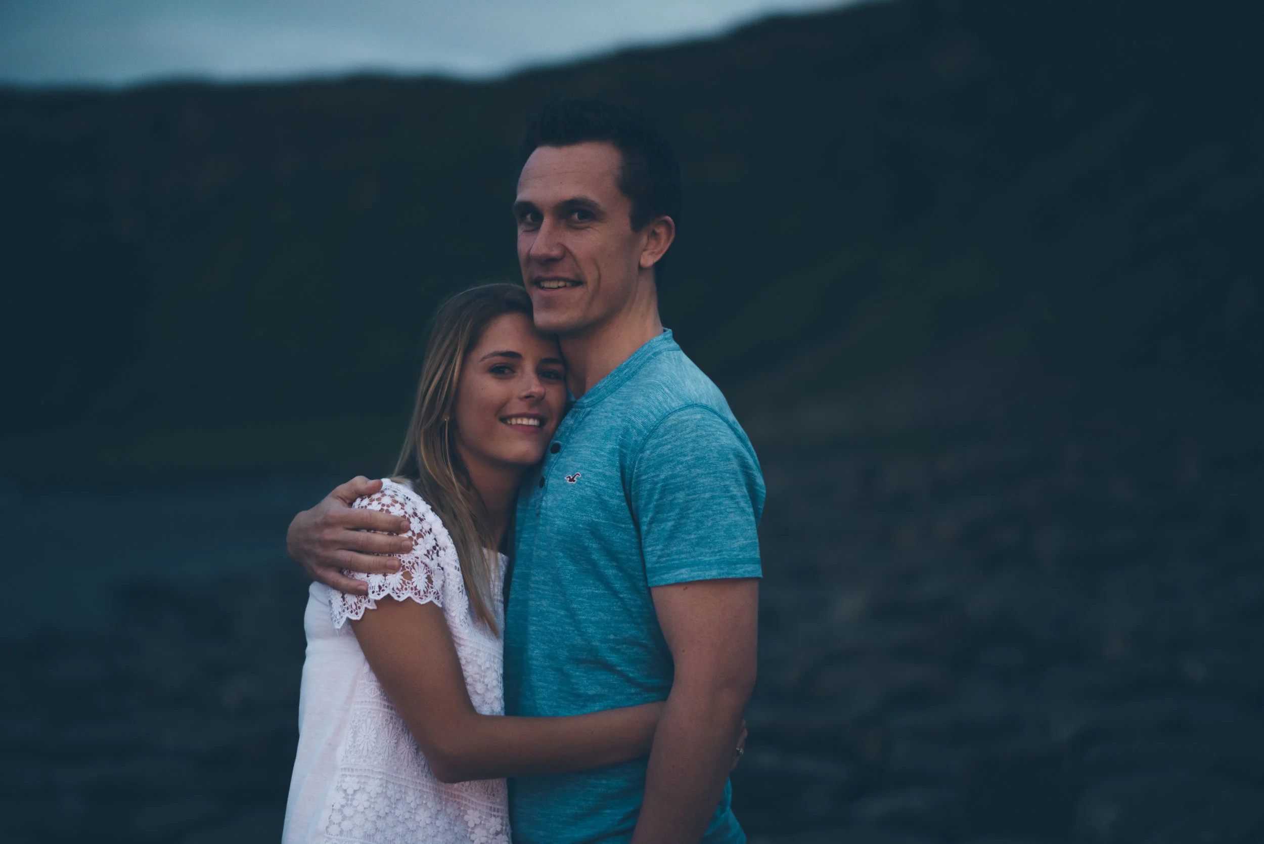 A young couple embracing on a dark outdoor landscape.