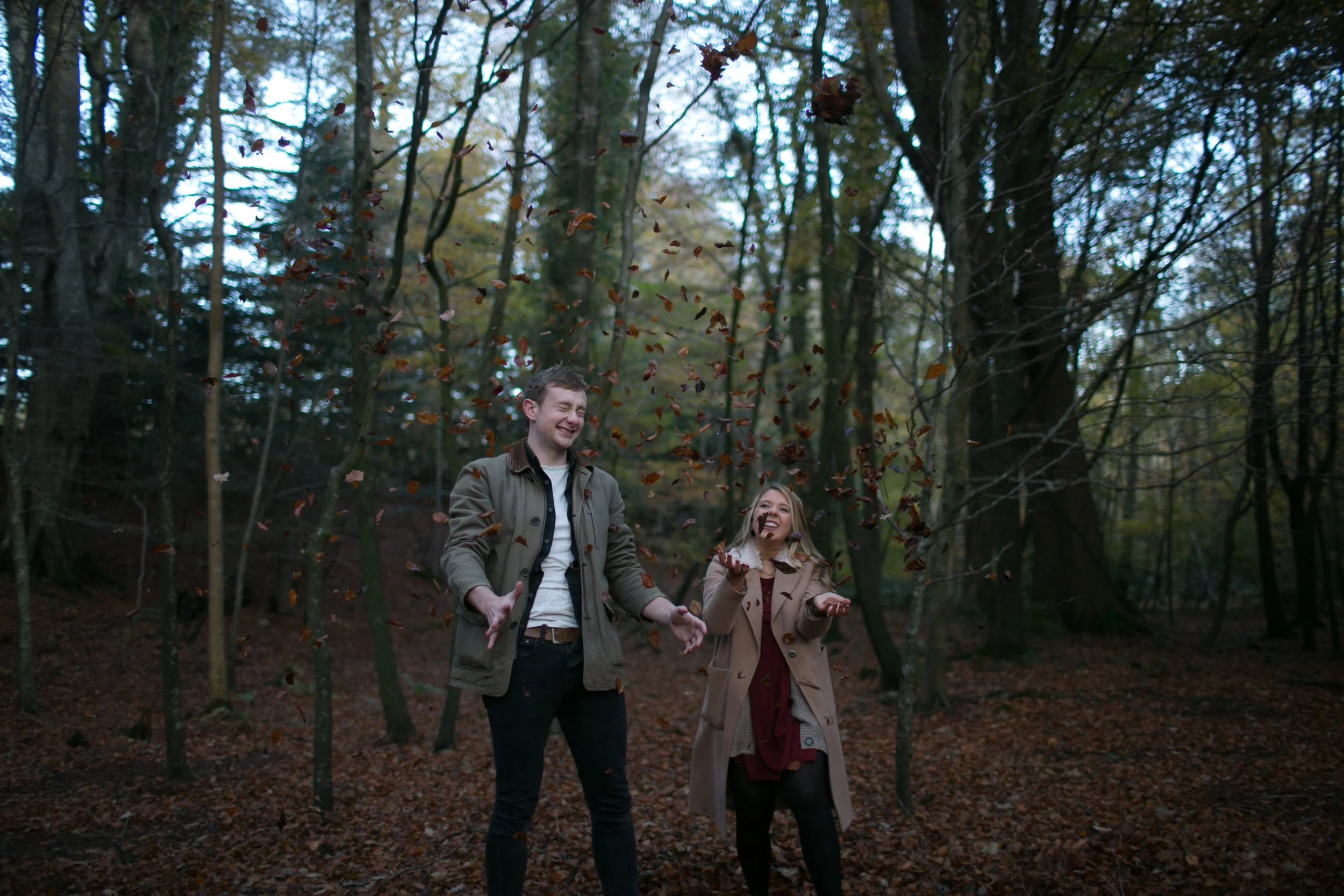 A man and a woman throwing fallen leaves in a forest during autumn.