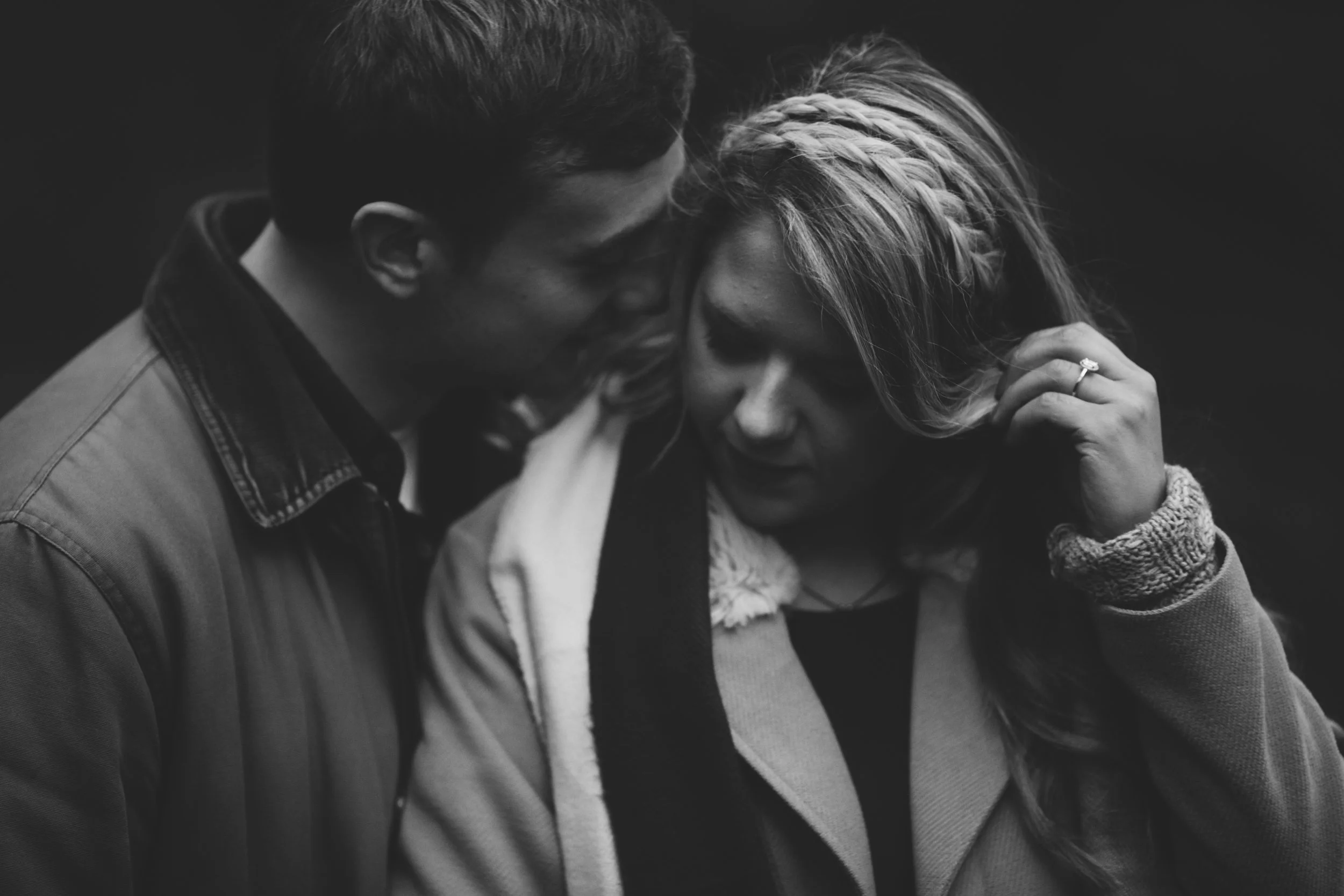 A black and white photo of a man and woman with their heads touching, eyes closed, and showing distress or sadness, with the woman holding her head and wearing a ring.