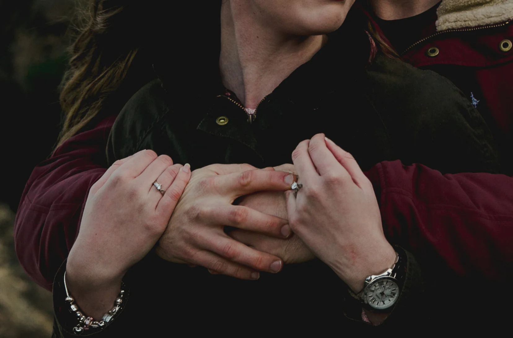 A woman and a man holding hands on her chest, with the woman wearing rings and a bracelet and the man wearing a watch, close-up shot.
