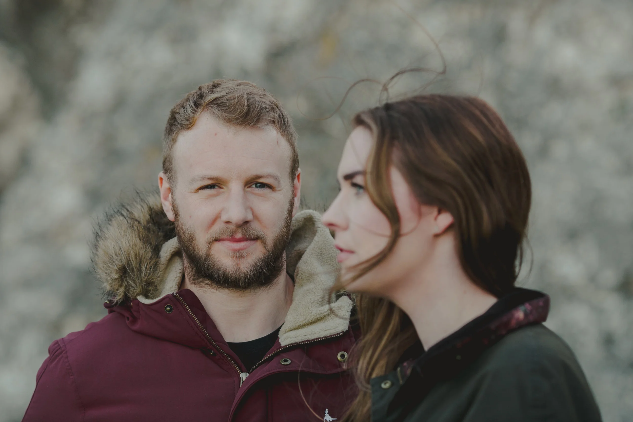 A man with a beard and a woman with long brown hair outdoors, with a blurred natural background.