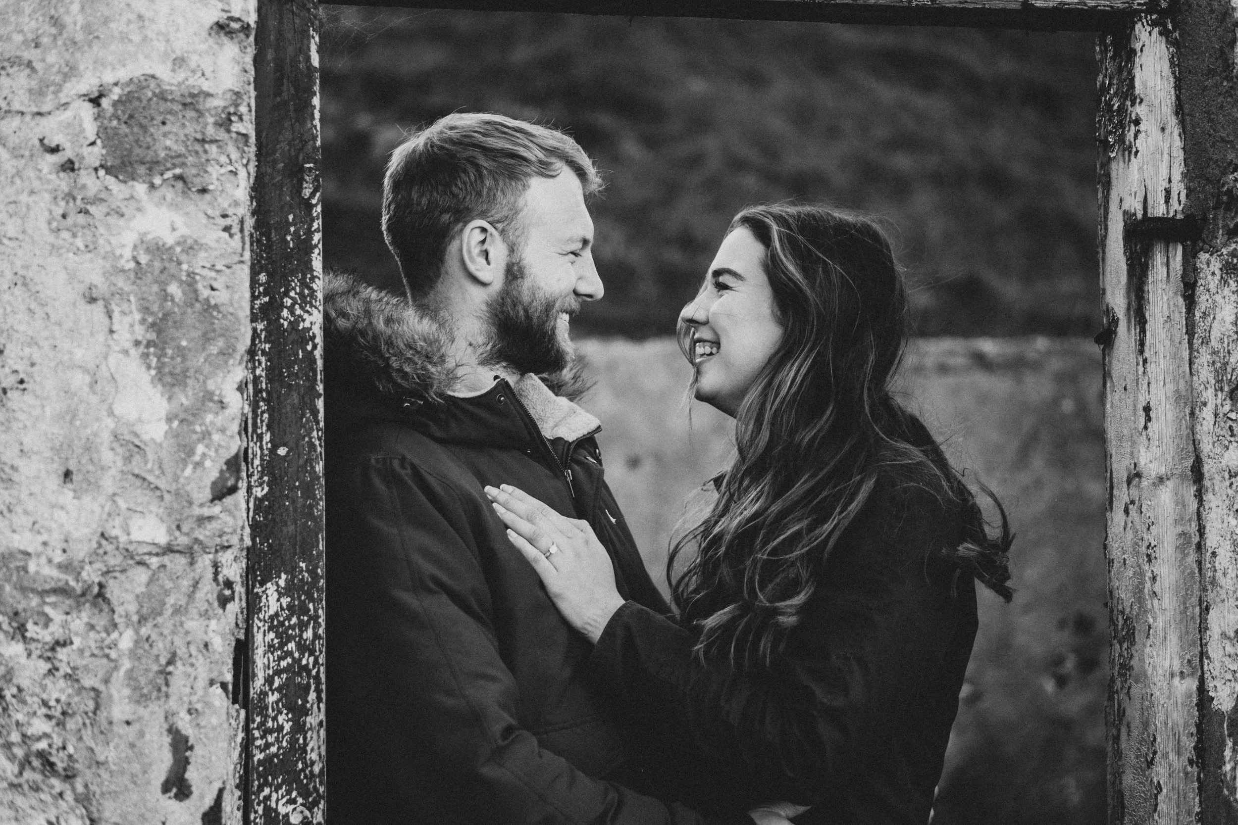 A couple smiling and looking into each other's eyes through a doorway in an outdoor setting, black and white photo