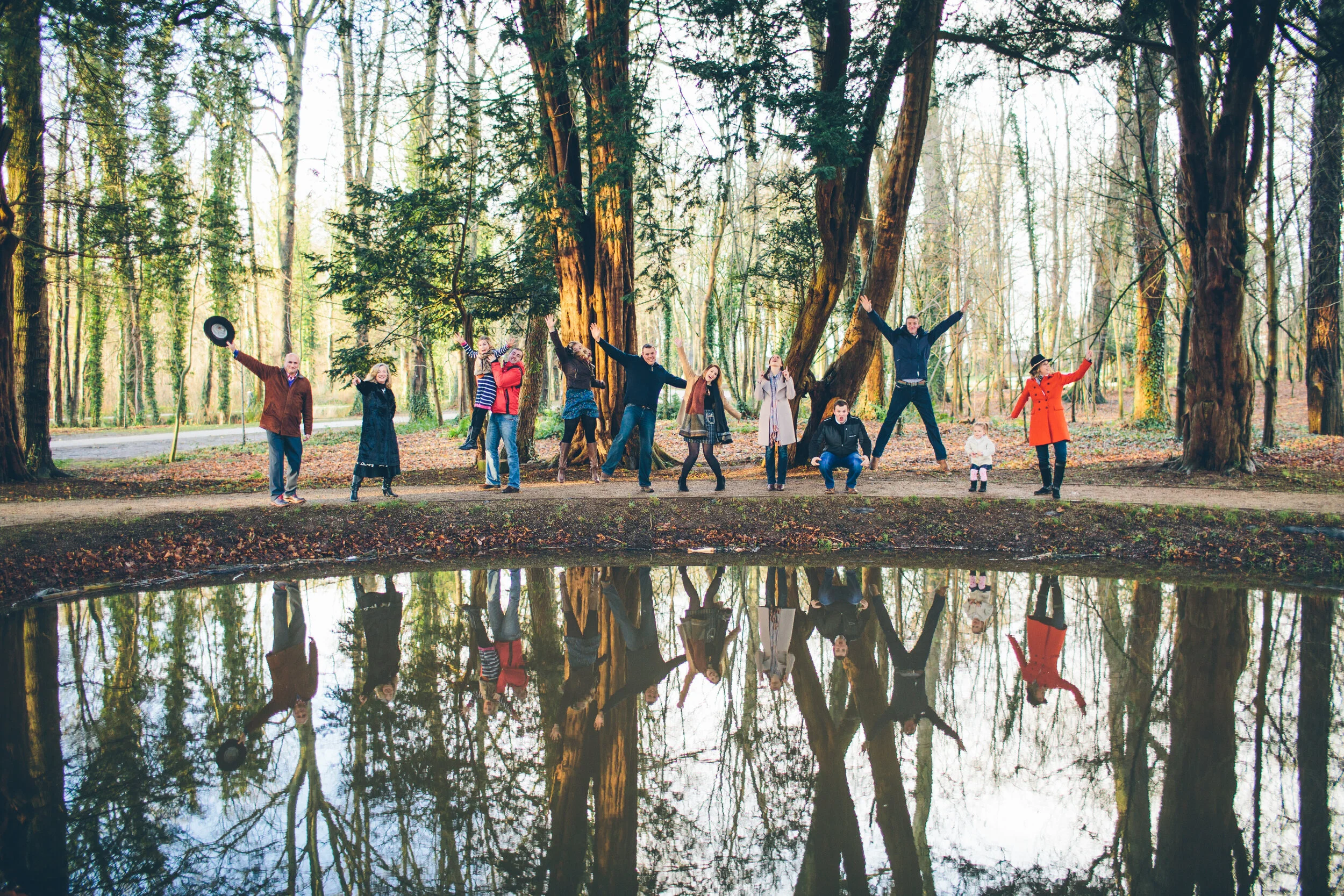 Group of people standing next to a pond in a forest, with their reflections visible in the water.