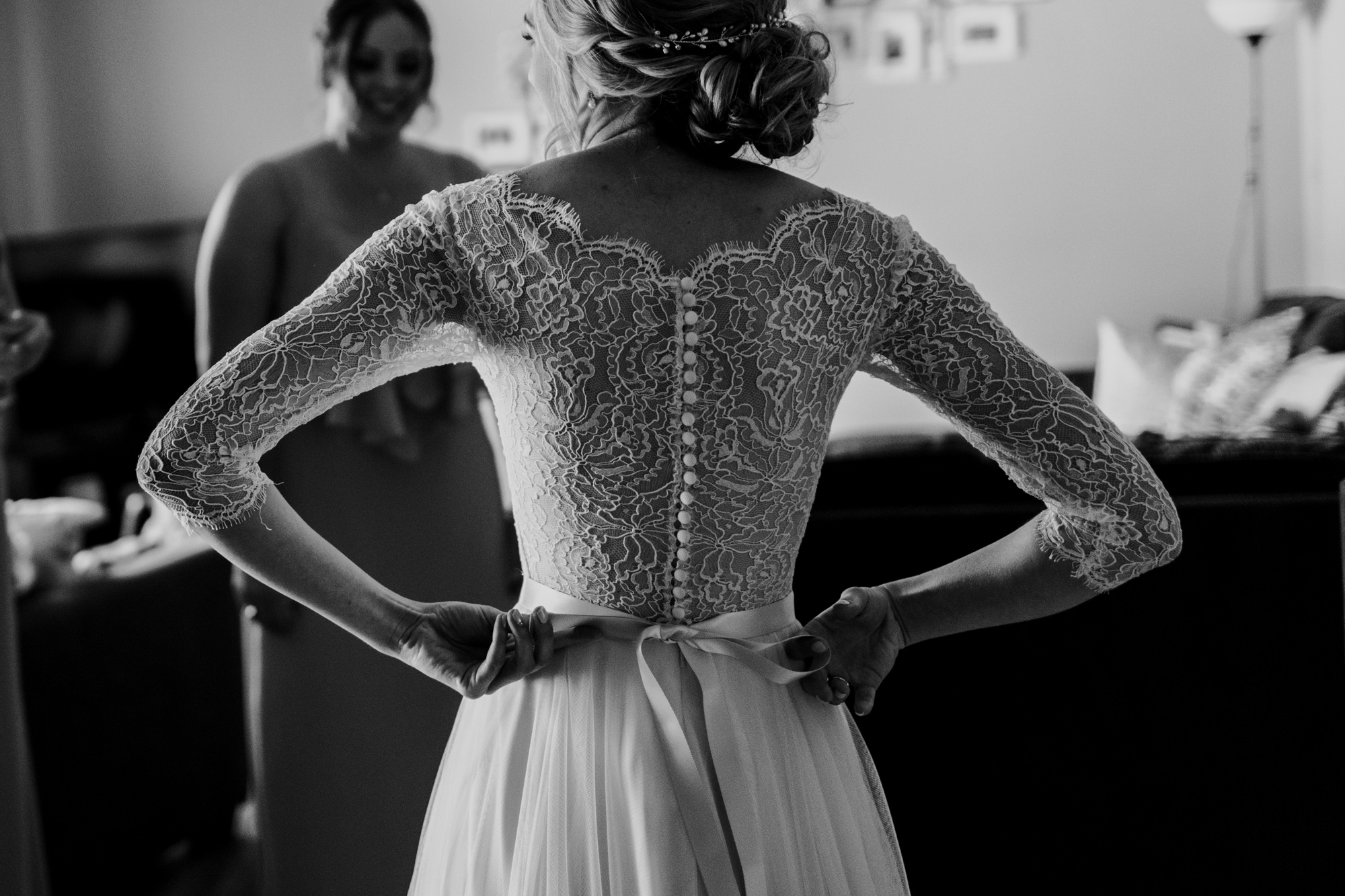  a bride is tying her dress with beautiful lace sleeves 