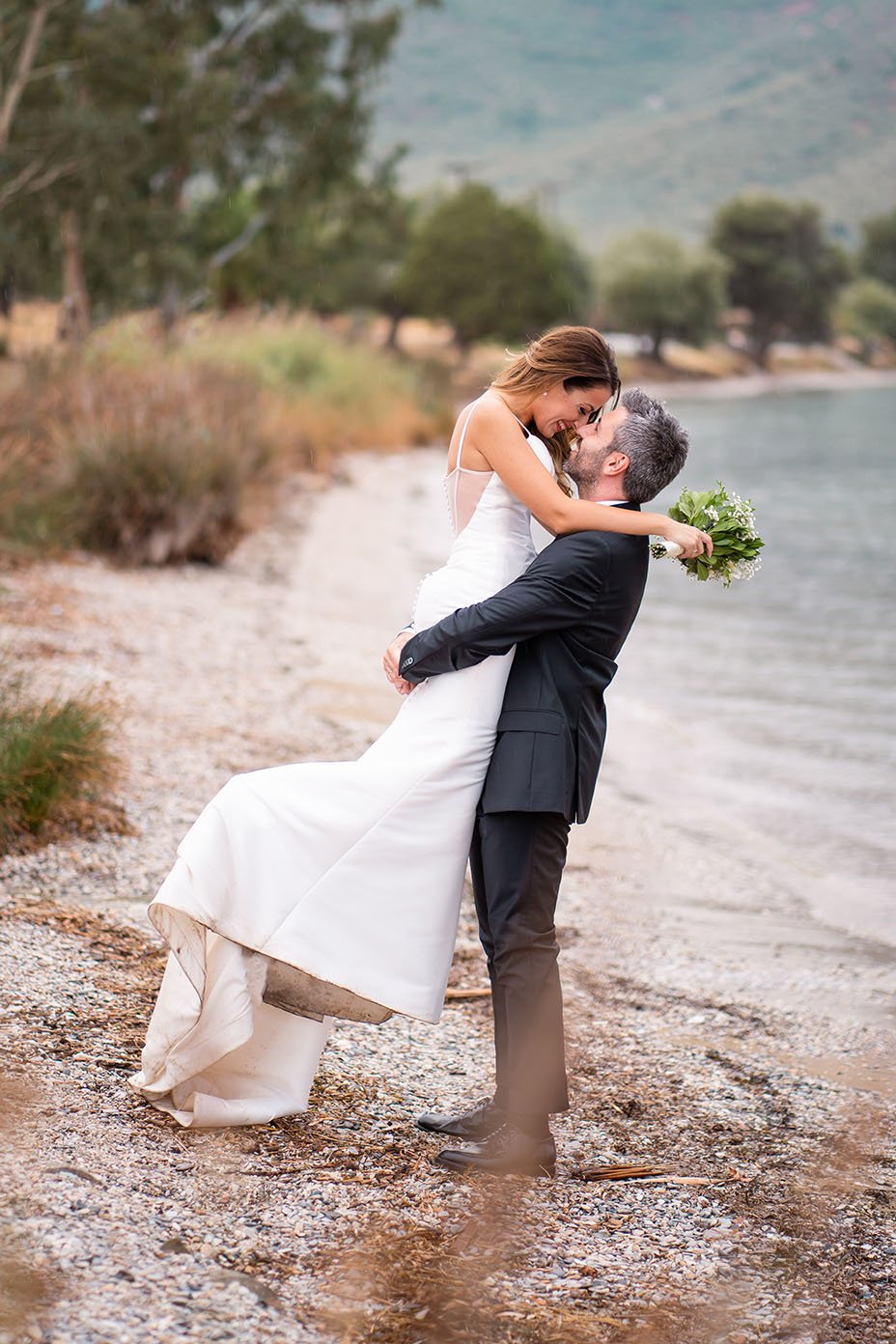  In this stunning wedding photo taken in Pelion, Greece, the groom held his bride high in the air, their joy and love for each other radiating from every pore. The bride, her wedding bouquet held firmly in her hand, laughed with delight as she looked