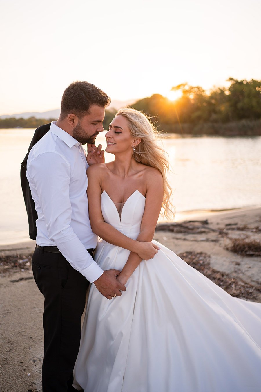  As the warm sun sets over the tranquil beach, the bride and groom share a tender moment, lost in the bliss of each other's company. With their eyes closed and a gentle breeze blowing through their hair, they lean in for a passionate kiss, their love