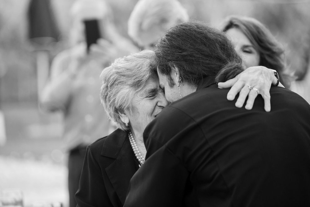  This black and white photo captures a tender moment between a groom and his grandmother on his civil marriage day. The groom leans his head gently against his grandmother's, their eyes closed in a moment of pure emotion. The love and affection betwe