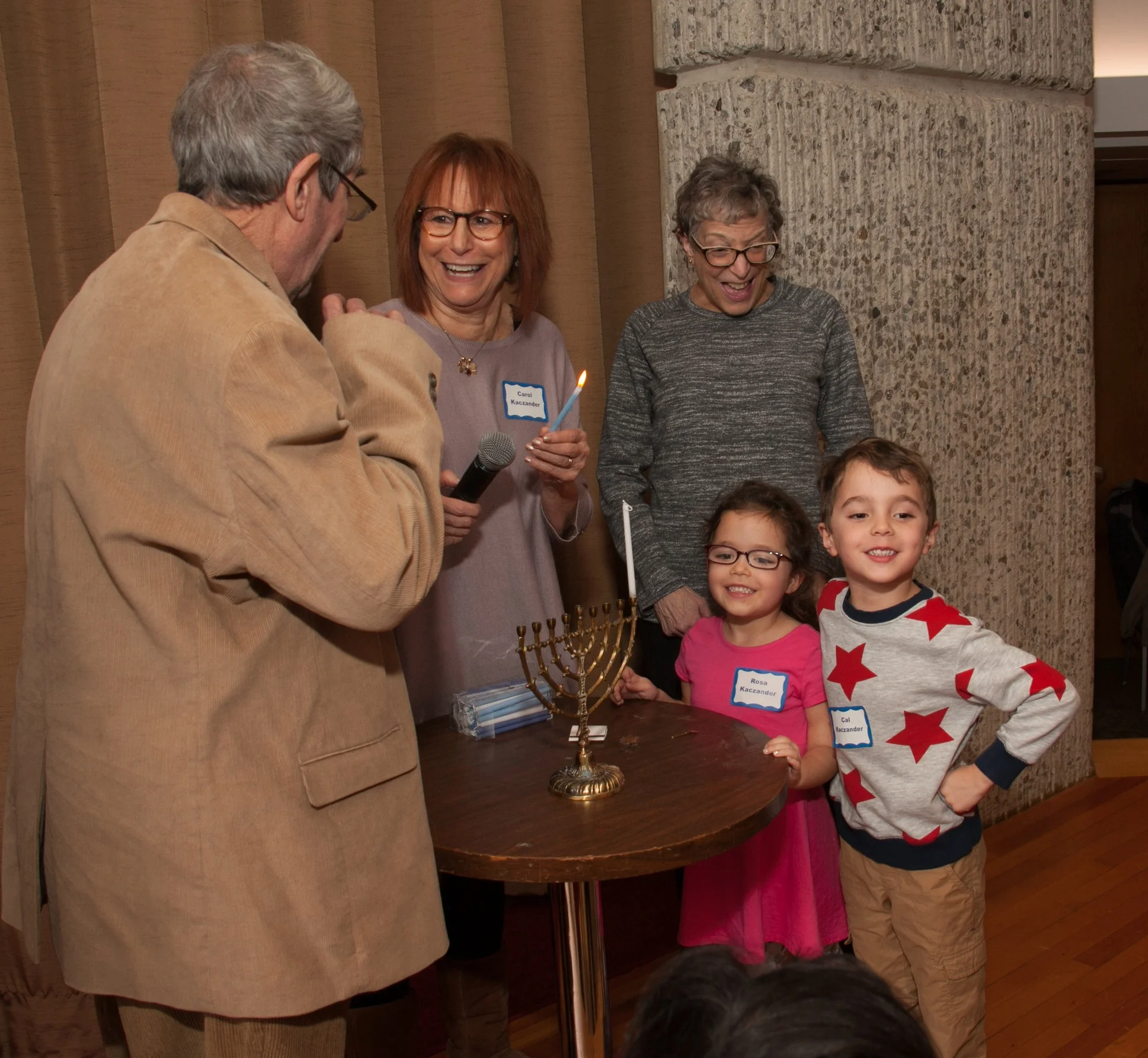 JARC Staff and family member Carol Kaczander and grandchildren Rosa and Calvin Kaczander lighting the Menorah at the annual Hanukkah Party with Jack Resnick and Marsha Kowal.