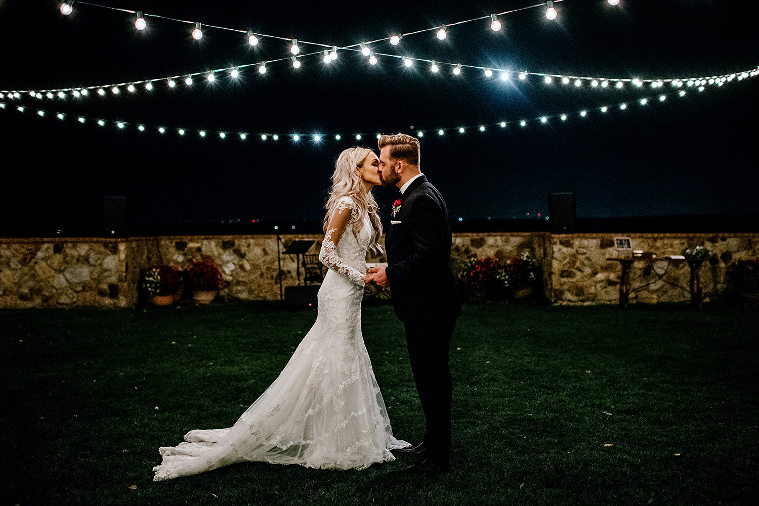 A night time portrait of a bride and groom kissing under hanging string lights at Bella Collina Florida