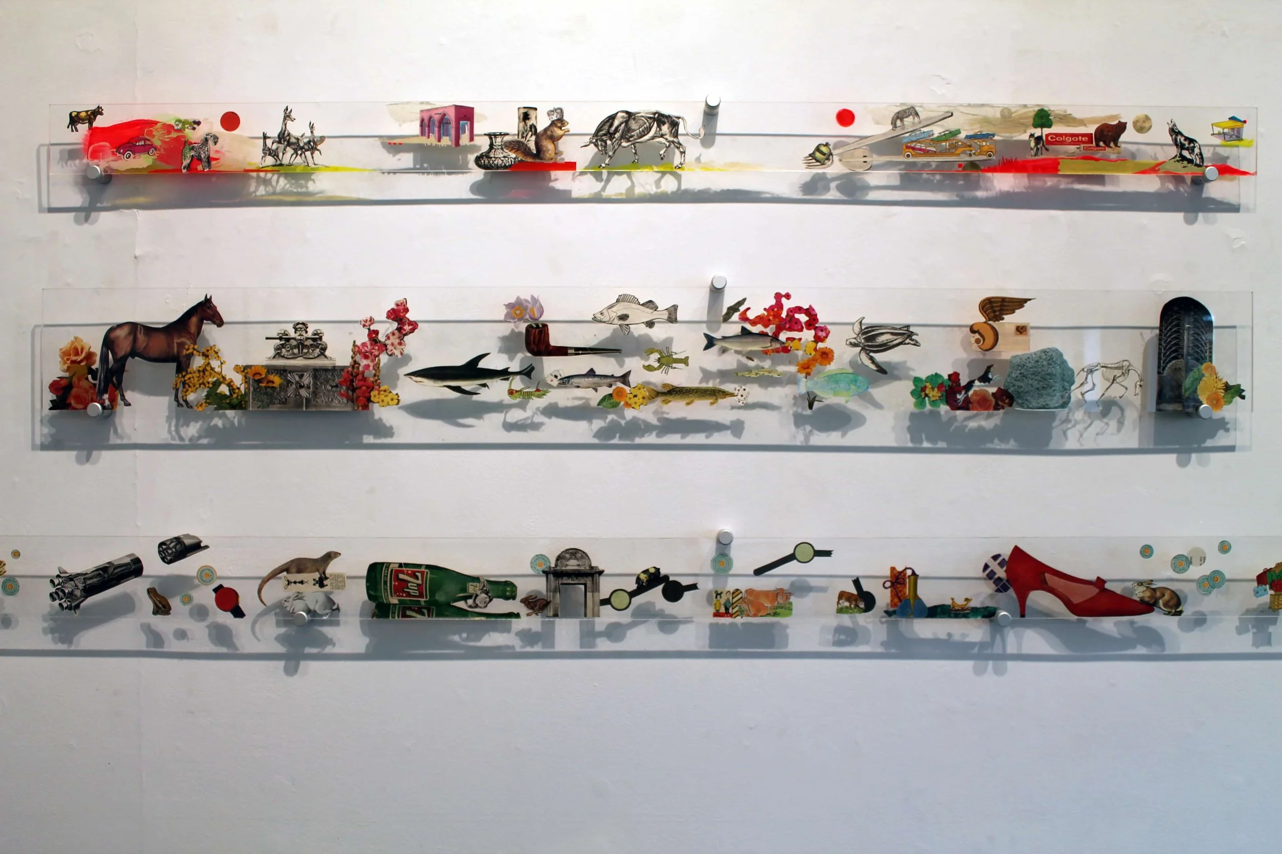 Three shelves on a white wall filled with various small objects including animal figurines, miniature structures, vehicles, flowers, and miscellaneous items.