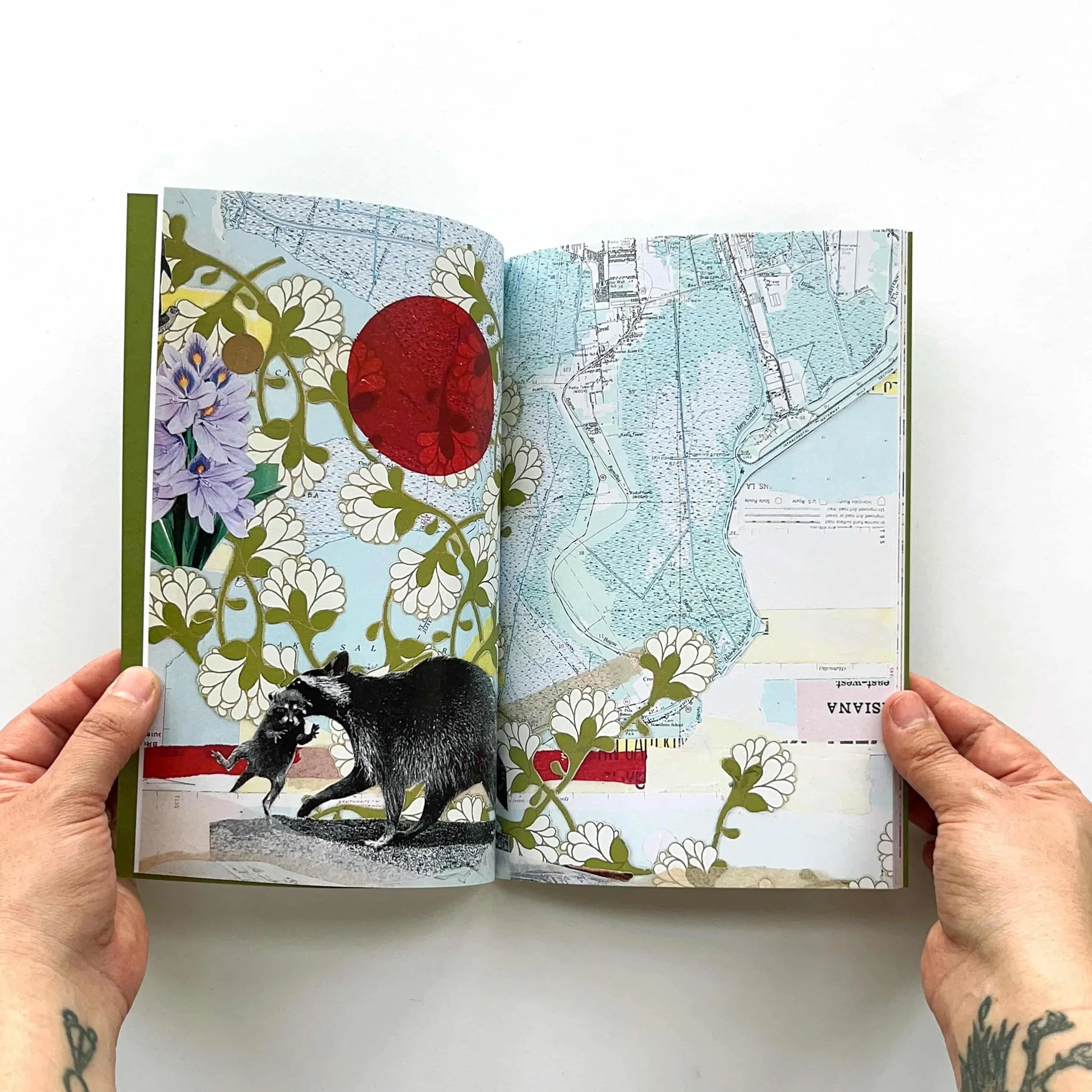 An open book with colorful illustrations and map pages, held open by two hands with tattoos on the wrists.