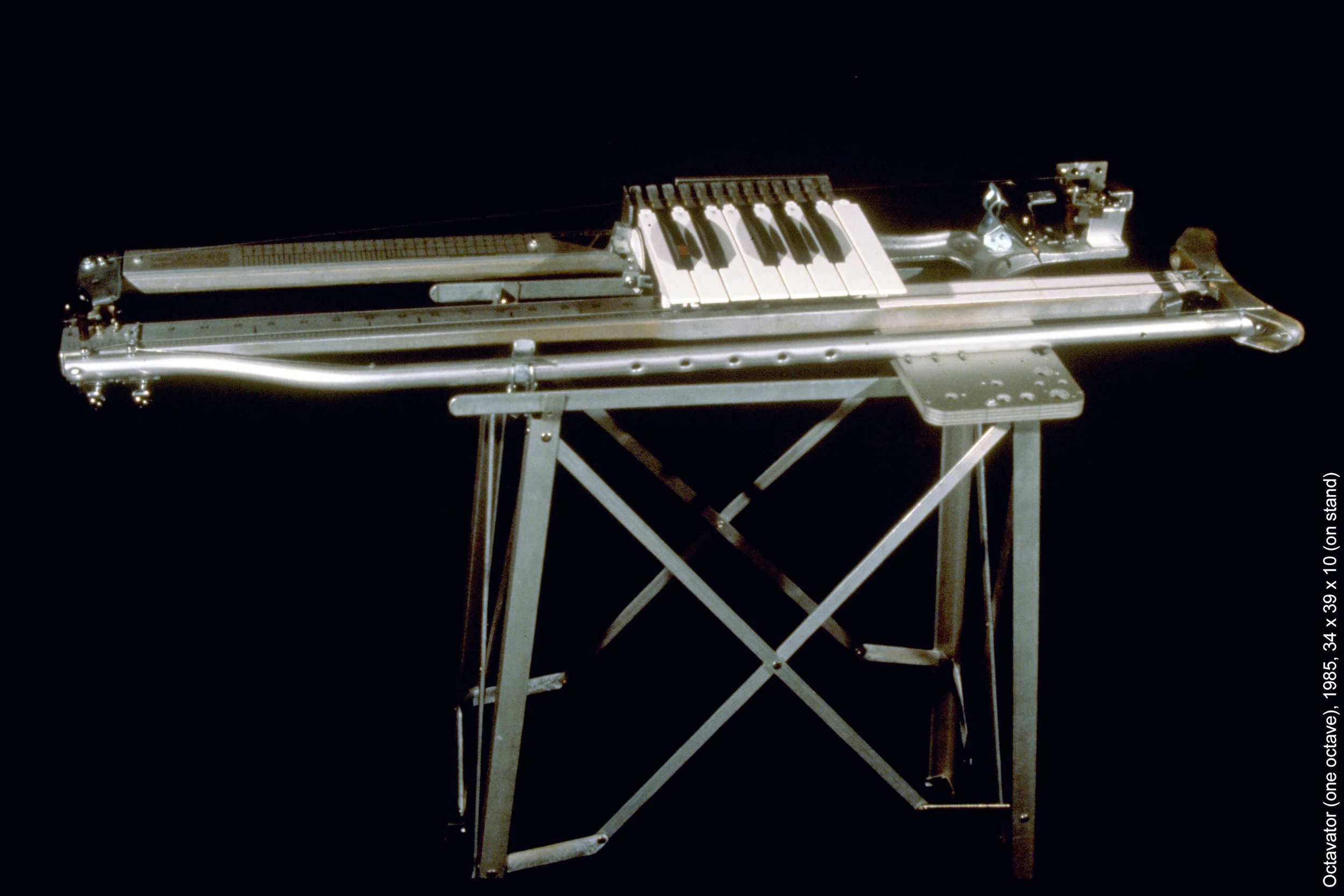 ‘Octavator’ (one octave), 1985, 34 x 39 x 10 (on stand). The Octavator uses one octave of keys with micro switches connected via telephone wires directly to the lamp inputs of six Carousel slide projectors that are aimed to the same area of the screen. Four keys trigger sequences of four slides that can be played live in any order. A master key advances all four slide projectors for the next group of four animated slides. The body of the Octavator is made from an aluminum crutch, a pneumatic door-closing mechanism, a shoe-size guide, ruler, and miscellaneous hardware in addition to the keyboard, It has four strings, two of which are fretted by the keyboard and/or plucking and bowing and is amplified with contact mics.’