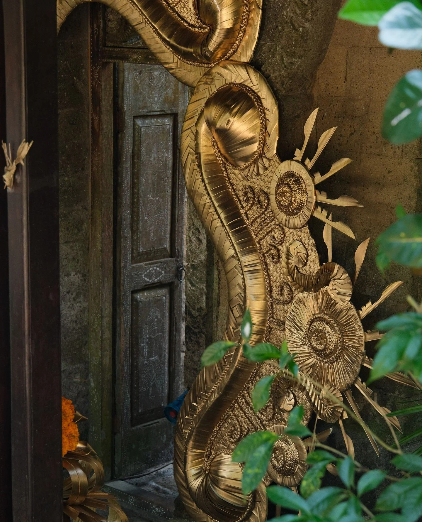 The textures of Bali: green glossy leaves, weathered wood with marks from carvers past, mud brick walls, and ornately woven dried leaf decor.