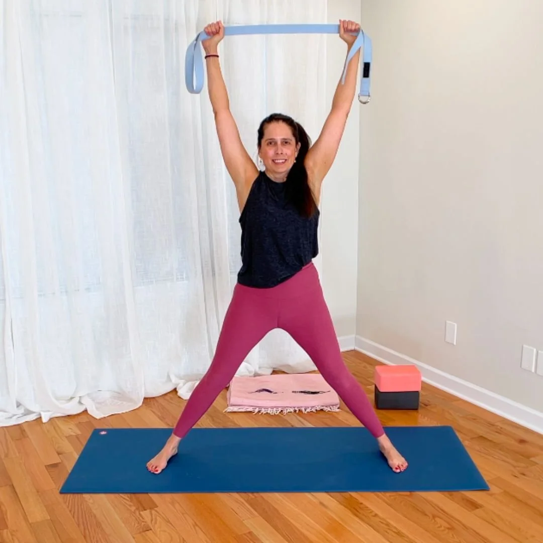 Yoga teacher standing with legs wide and holding a yoga strap overhead