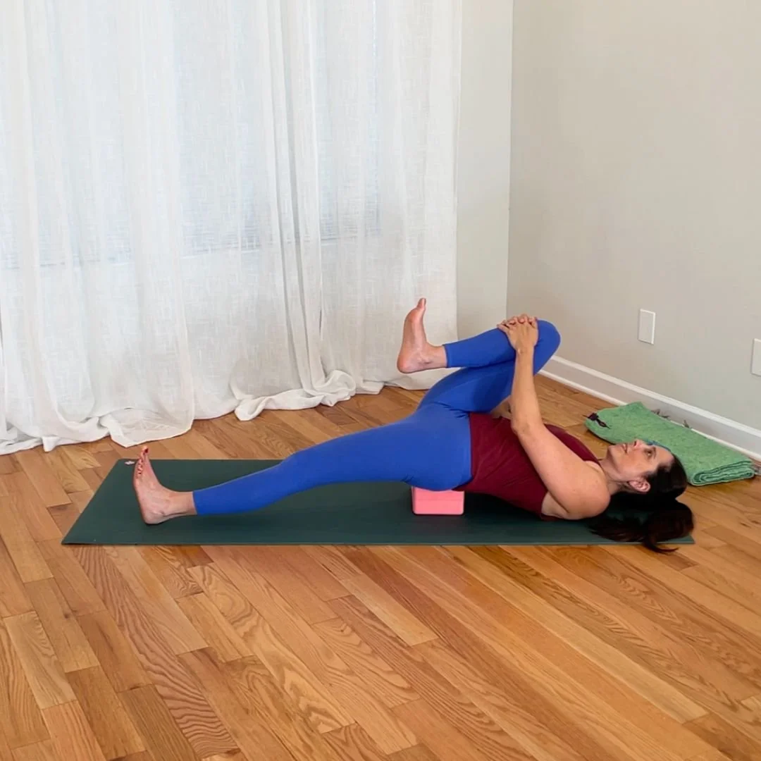 Supine hip flexor stretch with yoga block supporting pelvis and one knee drawn toward chest