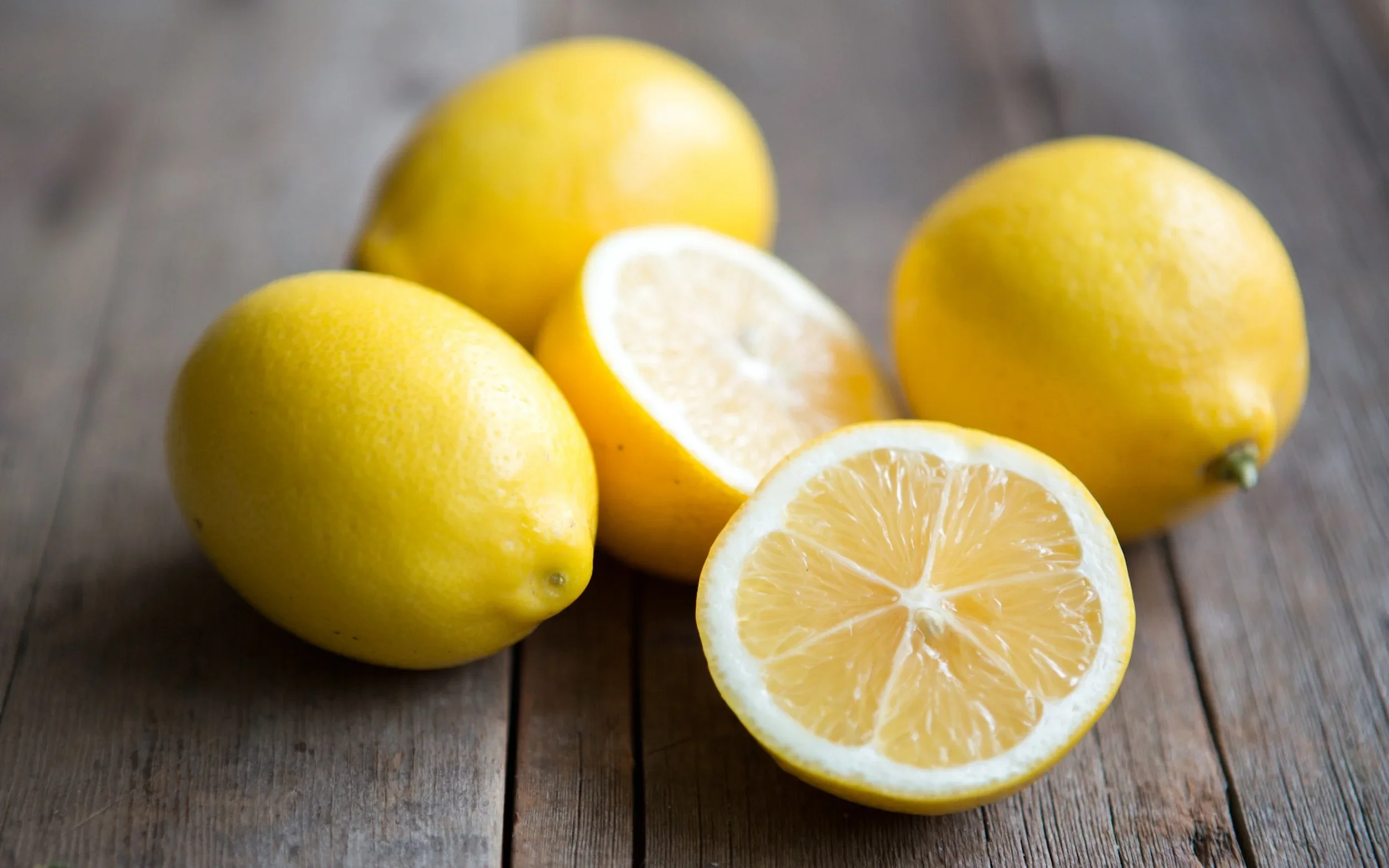 Whole and halved Meyer lemons on a rustic wooden table.