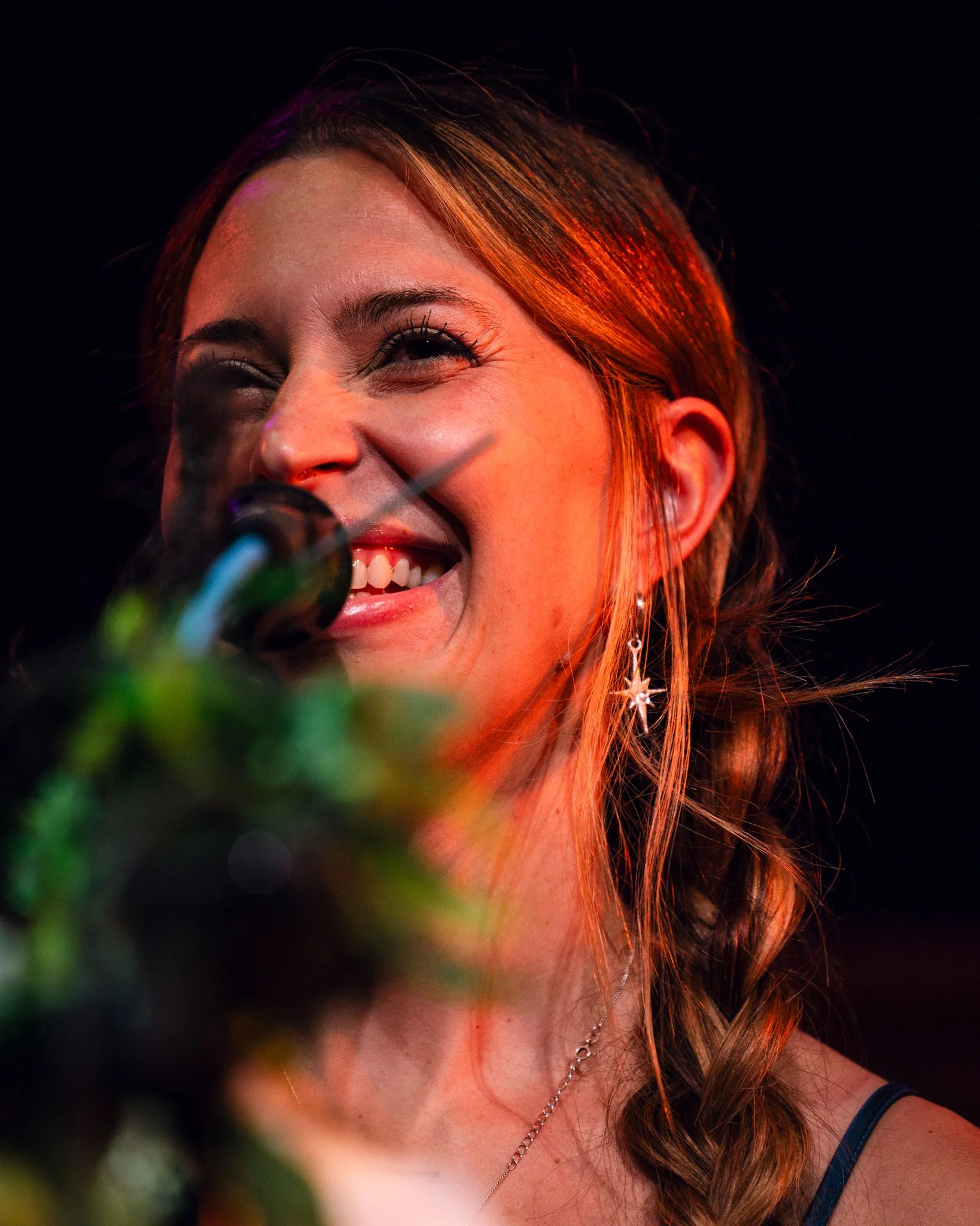 A woman with red hair and earrings smiling and singing into a microphone.