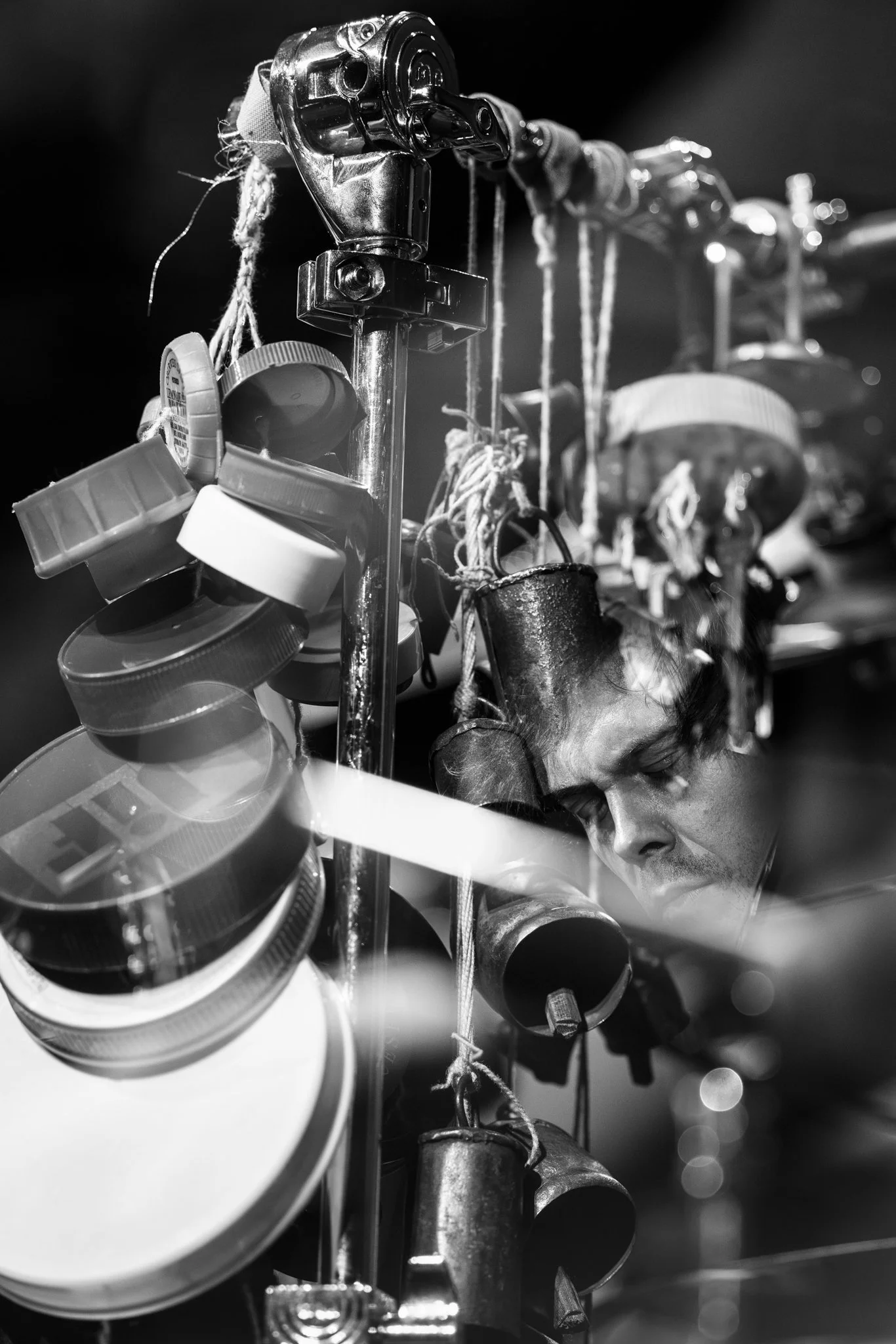 A man with closed eyes is hidden among hanging objects, including jars, lids, and ropes, on a display rack.