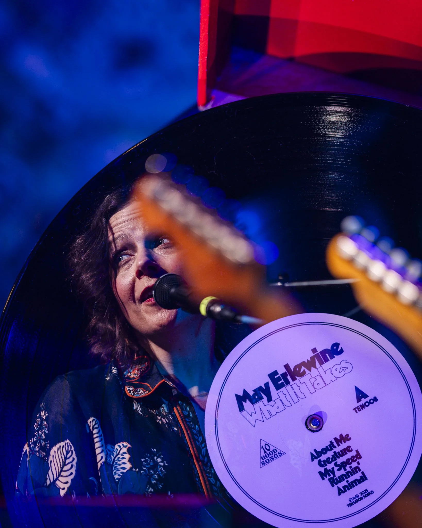 A woman singing into a microphone surrounded by a vinyl record with the text 'MayE HayLine World Hit Talks' and song titles on a label.
