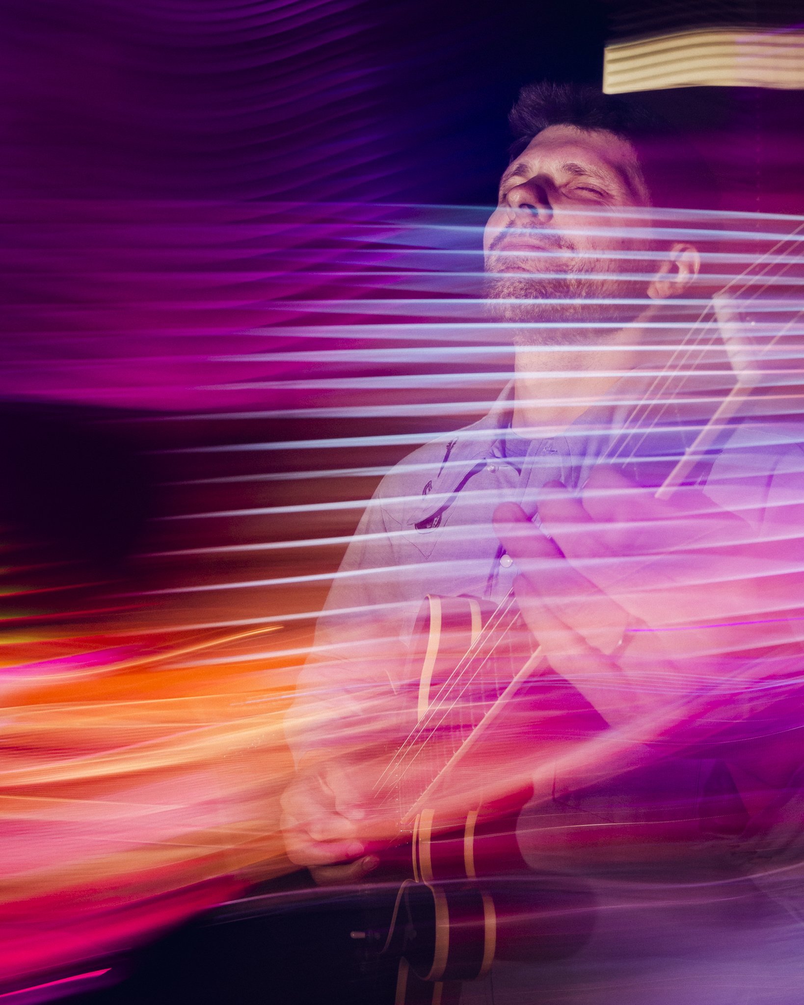 A man playing an acoustic guitar with colorful light streaks creating a vibrant background.