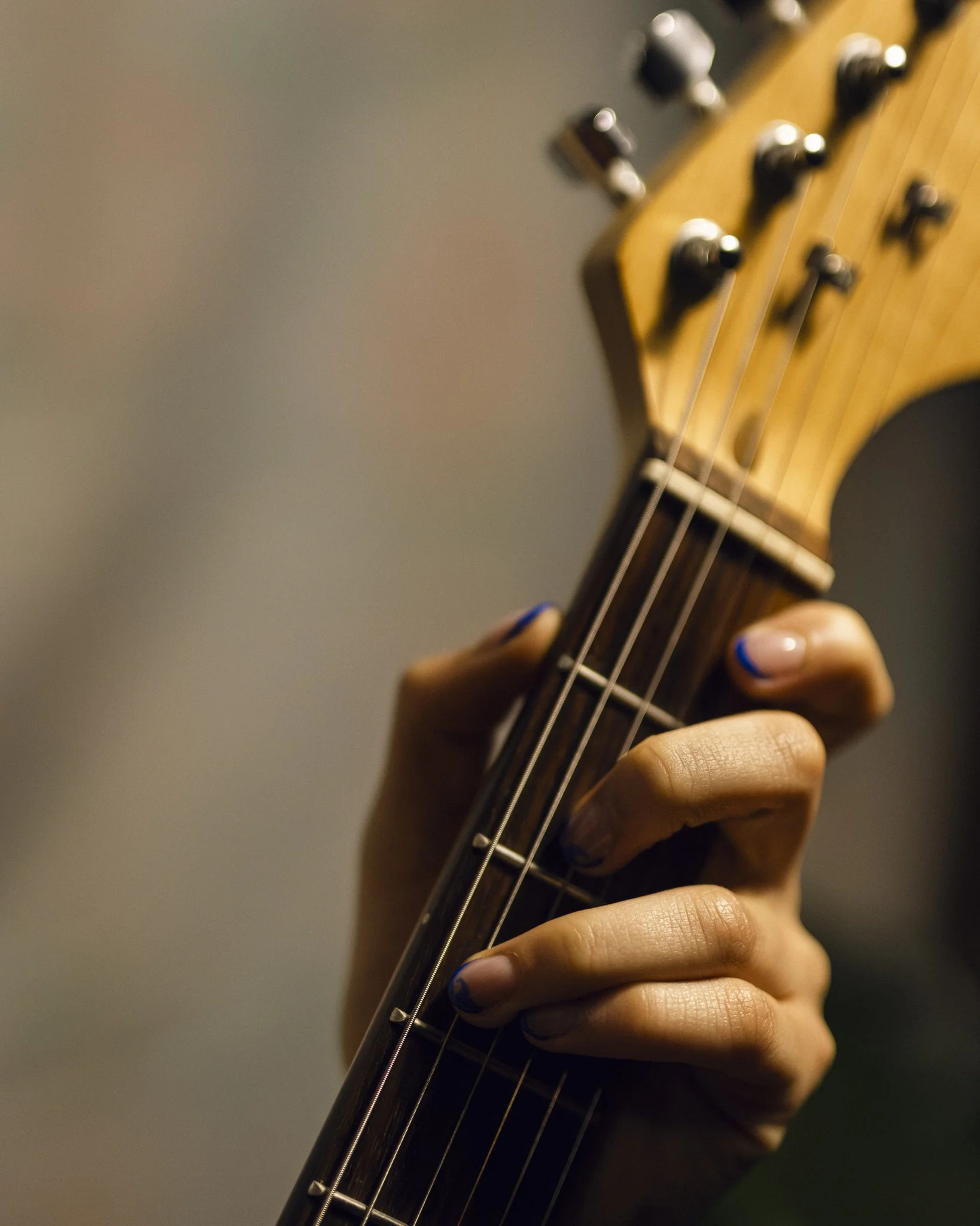 Close-up of a person’s hand pressing down on guitar strings on the fretboard of an acoustic guitar.