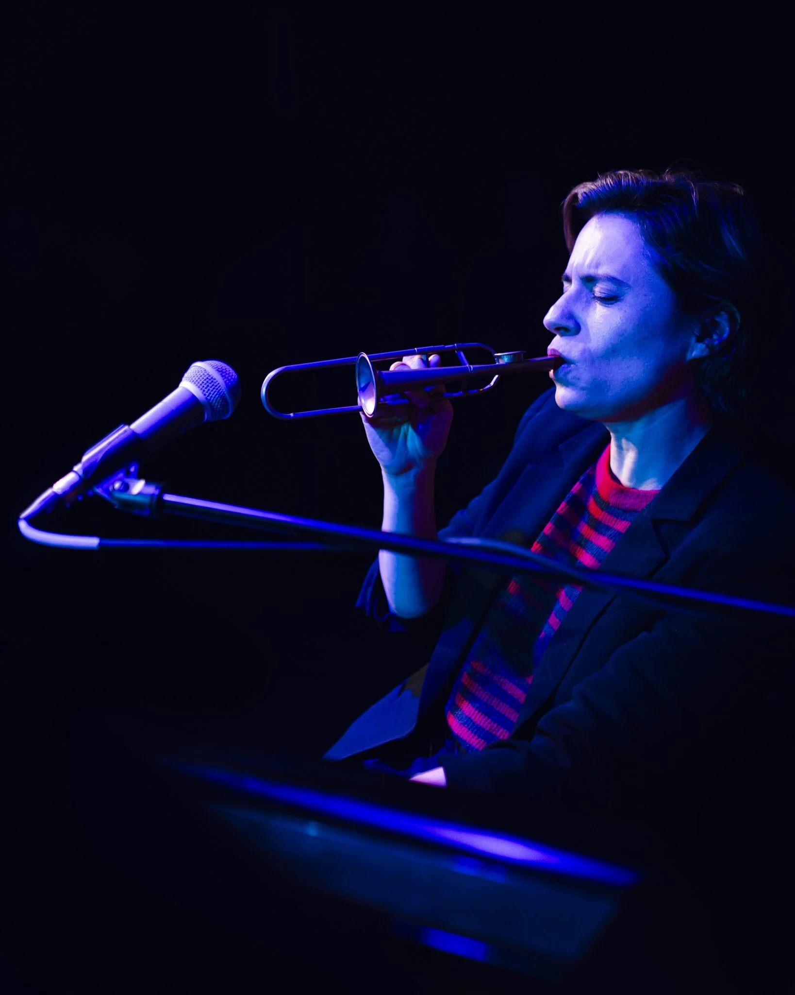 A woman playing a trumpet on stage, illuminated by blue and purple lights.