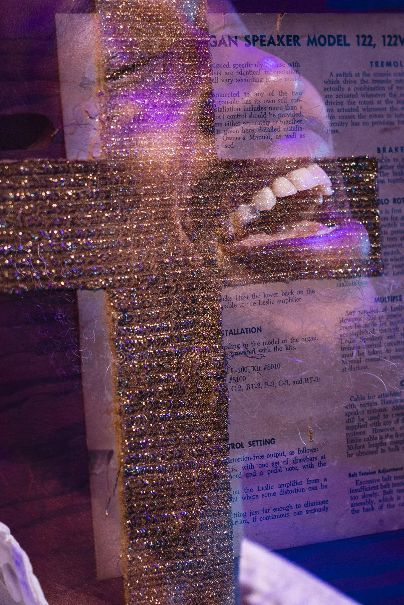 Close-up of a golden, shiny fabric over a printed manual page with partially visible text about a speaker model, illuminated with purple light.