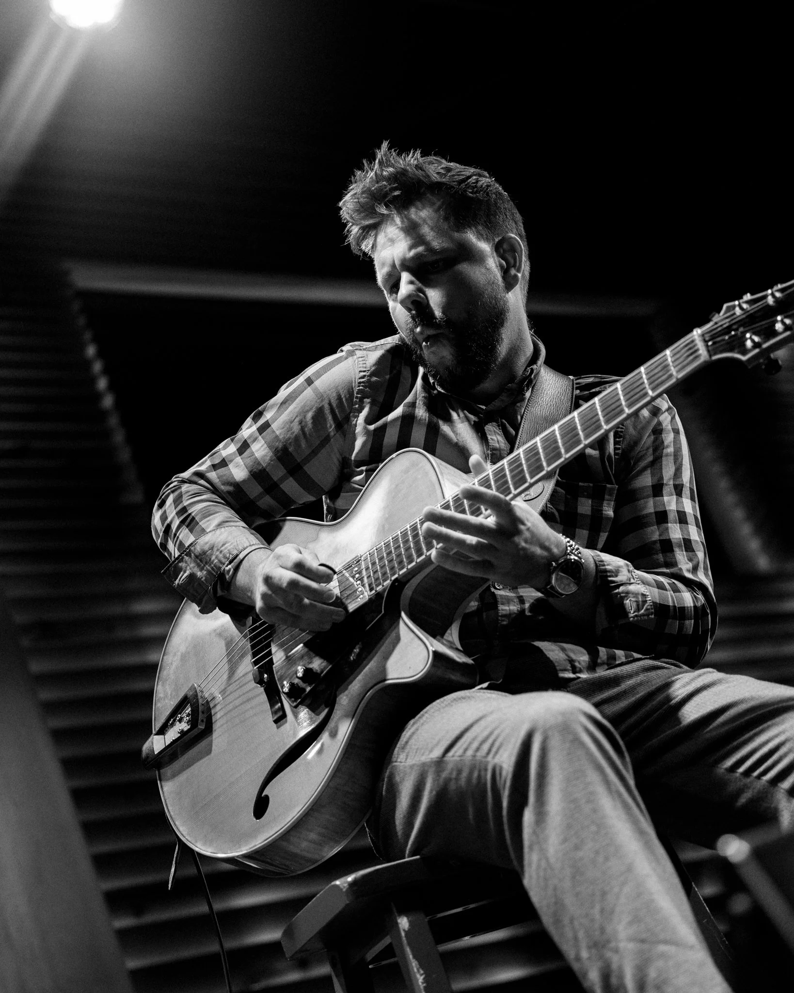 A man playing an acoustic guitar in a recording studio, black and white photo.