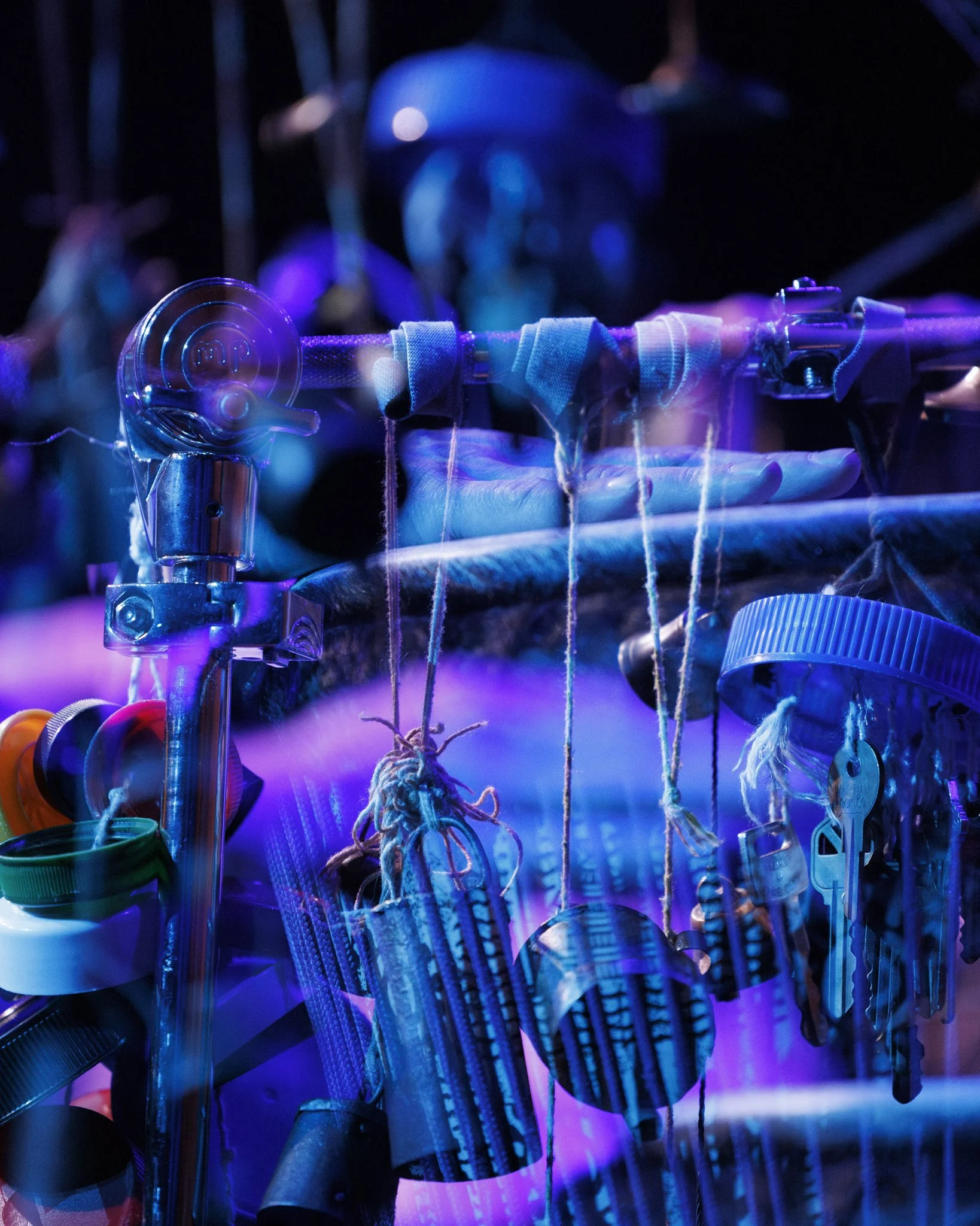 Close-up of a guitar stand with various objects hanging from it, illuminated by purple and blue stage lights.