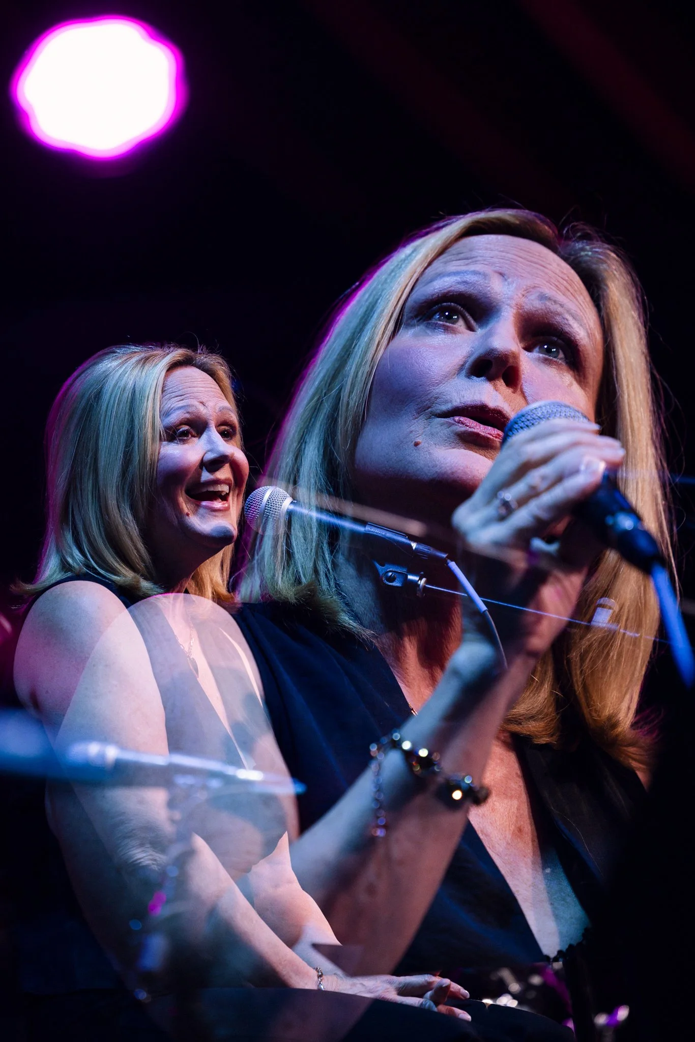 A woman with blonde hair holds a microphone and sings on stage, with dynamic lighting and visible double exposure effect.