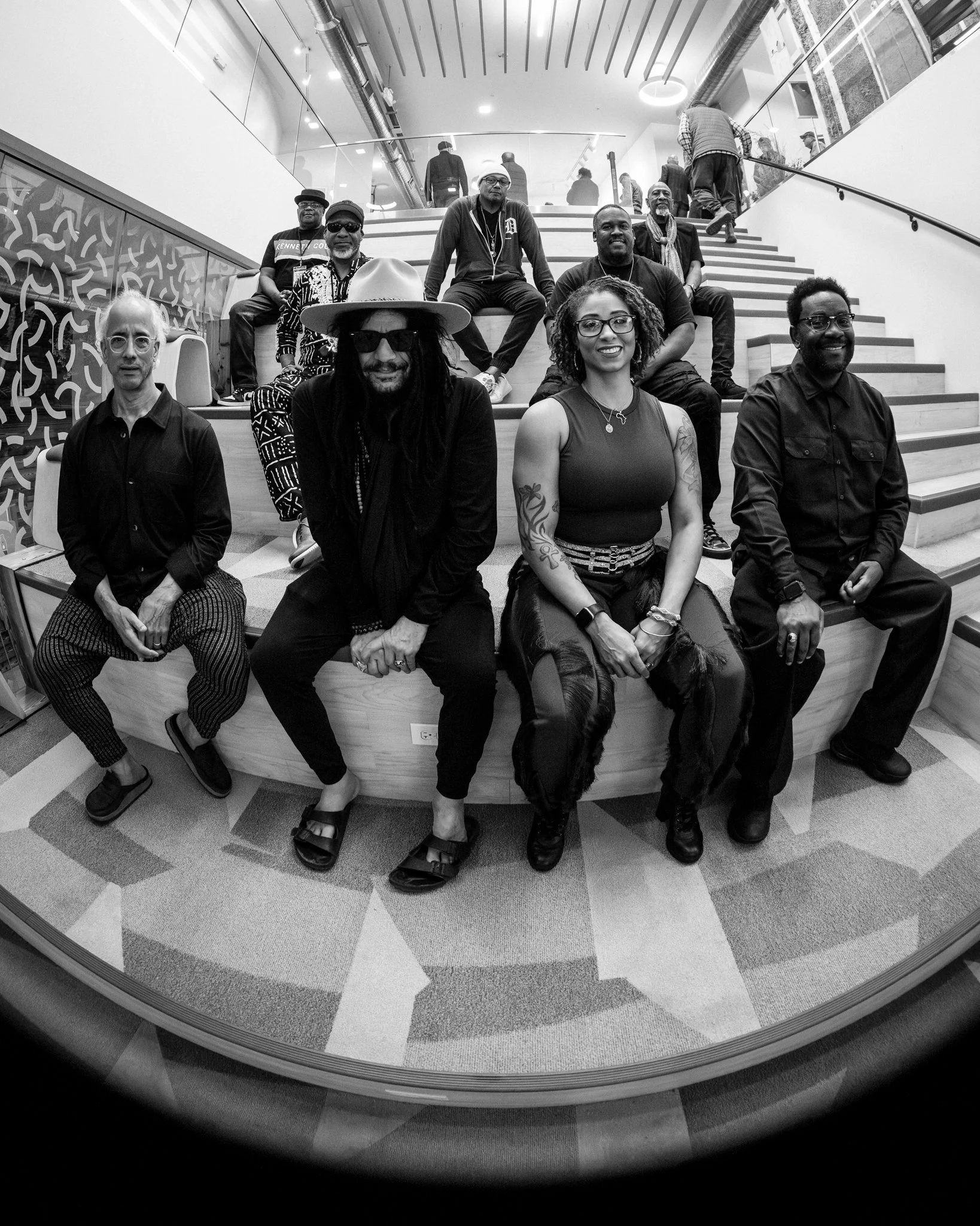 Group of ten diverse people sitting and standing on stairs inside a modern building, some smiling at the camera.