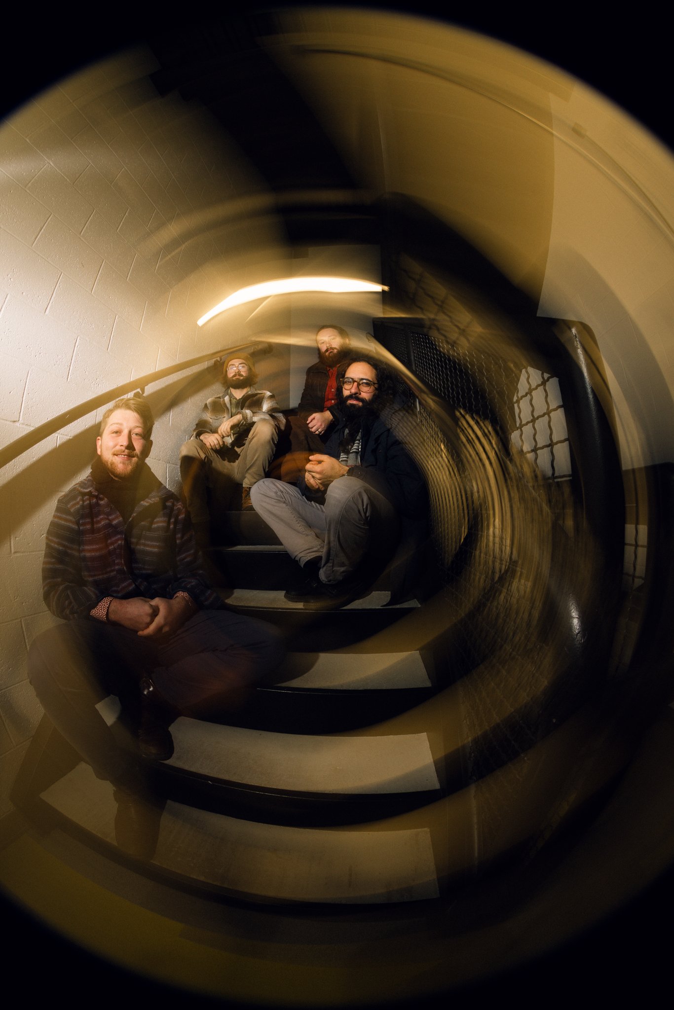 A group of five men sitting on a staircase, viewed through a fisheye lens, creating a swirling effect.