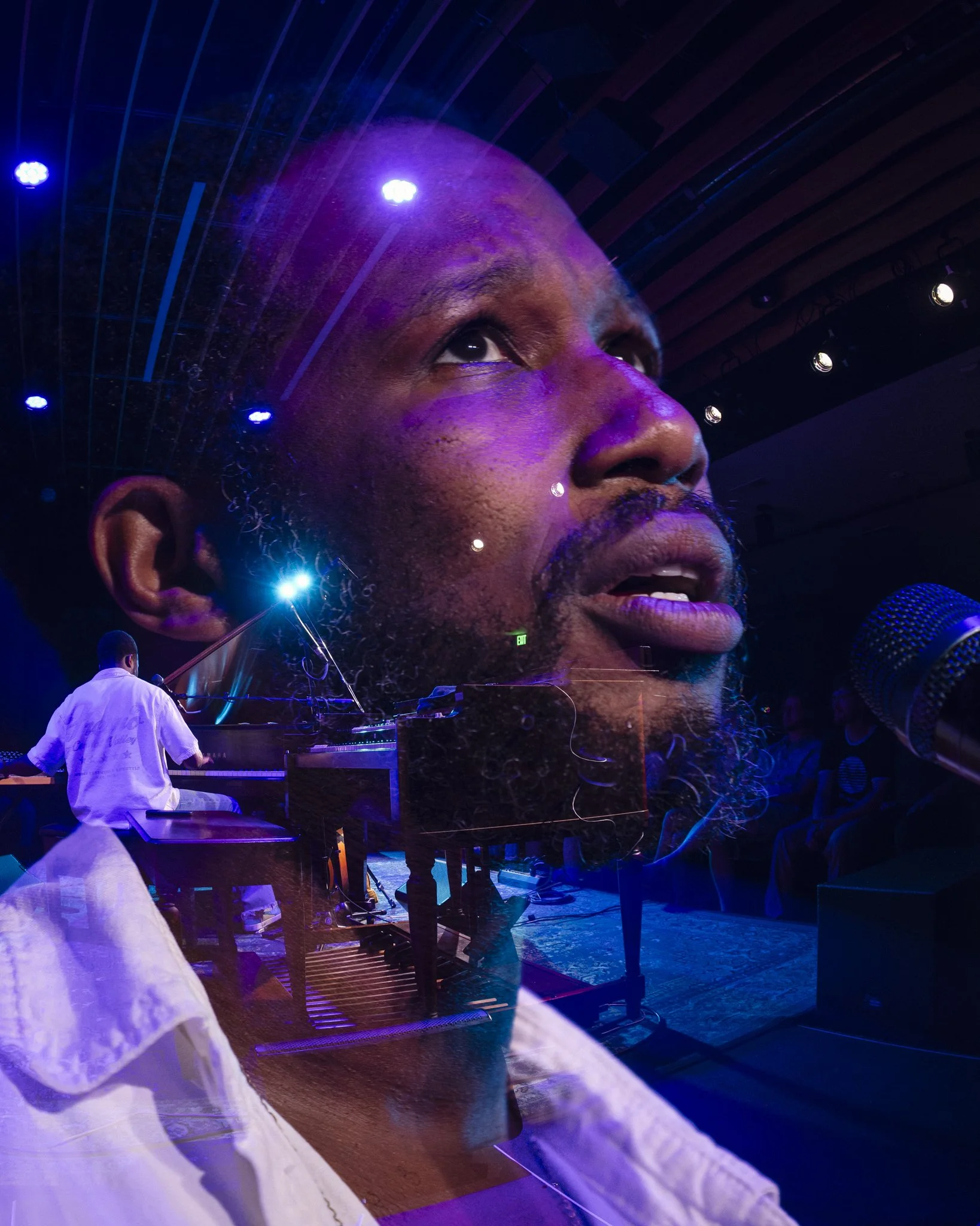 A performer singing on stage with a massive superimposed image of a man's face and a pianist playing piano.