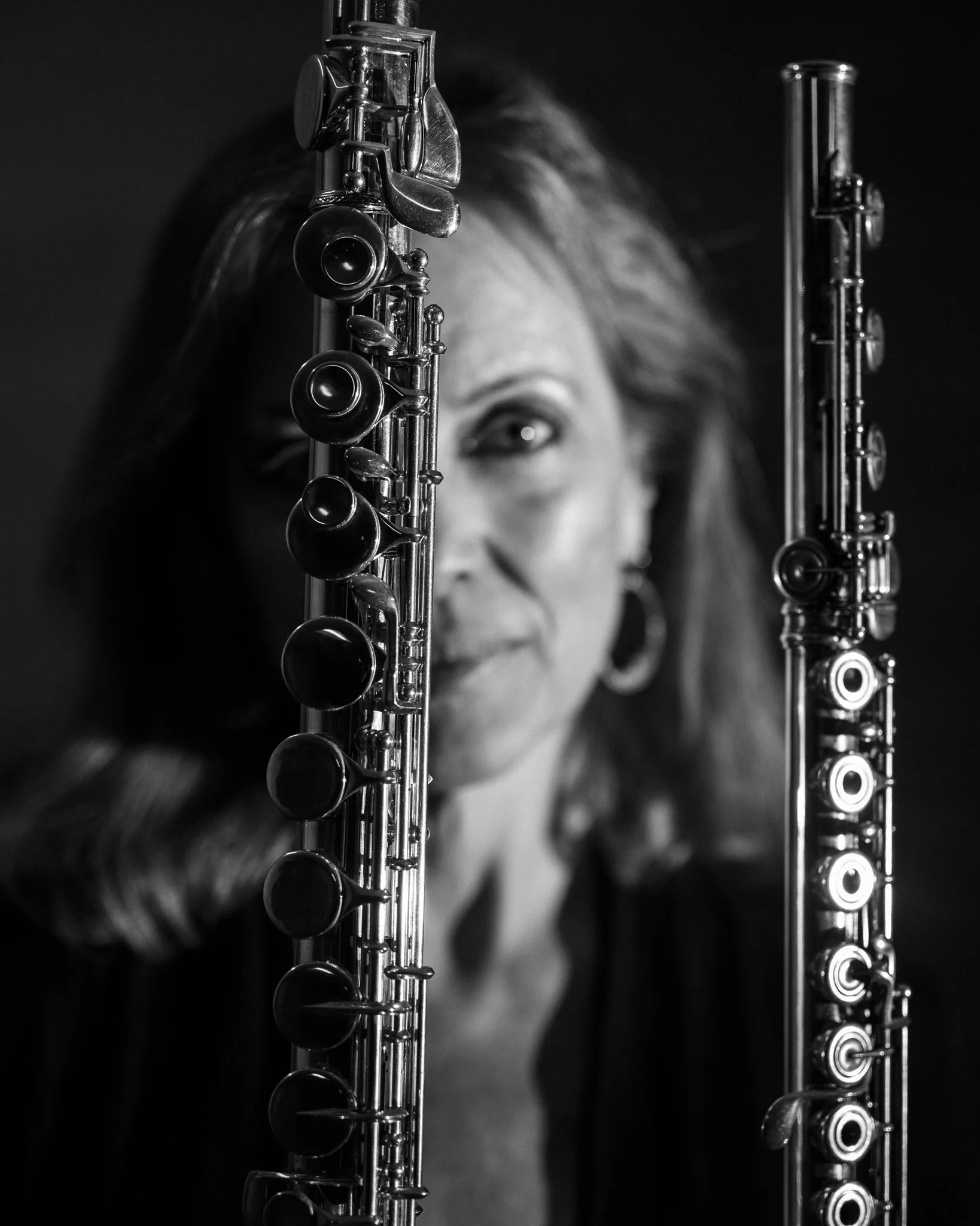 A woman holding two black and silver flutes, partially obscuring her face, in a black and white photograph.