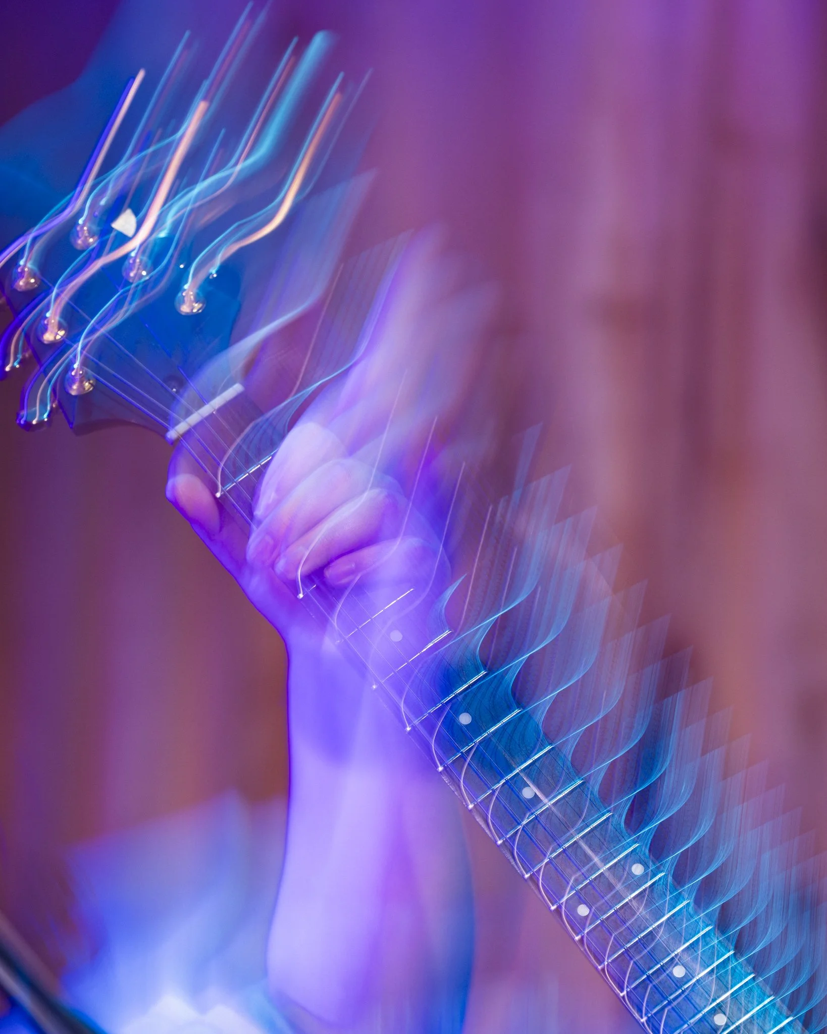 A hand holding a guitar neck, with motion blur and colorful lights creating an abstract, vibrant effect.