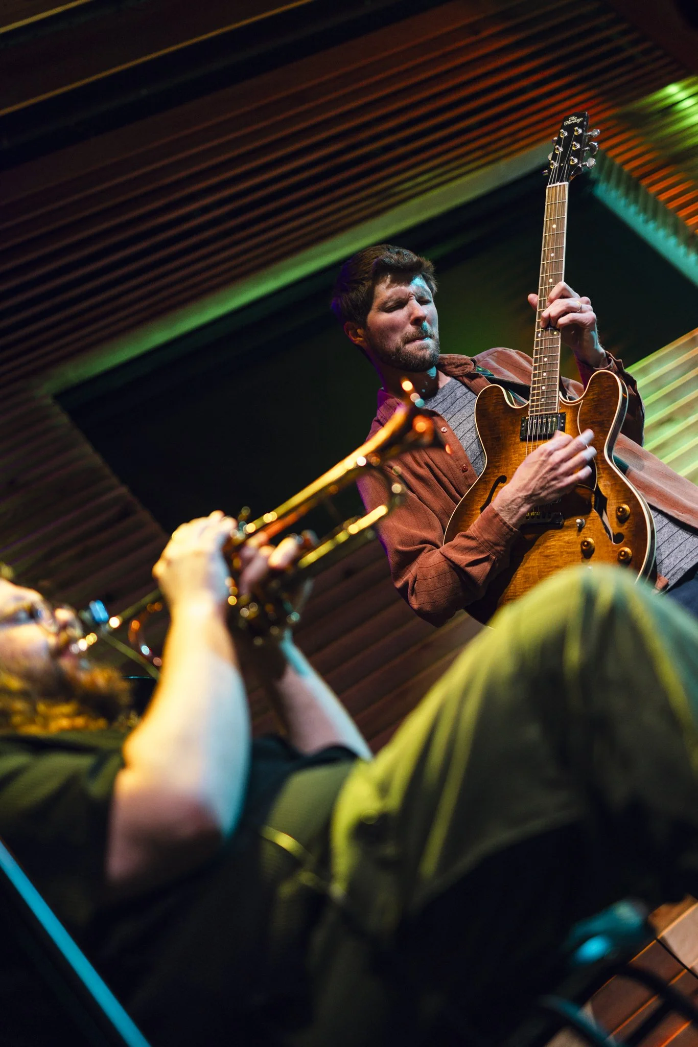 Musicians playing guitars in a dimly lit venue with colorful stage lighting.